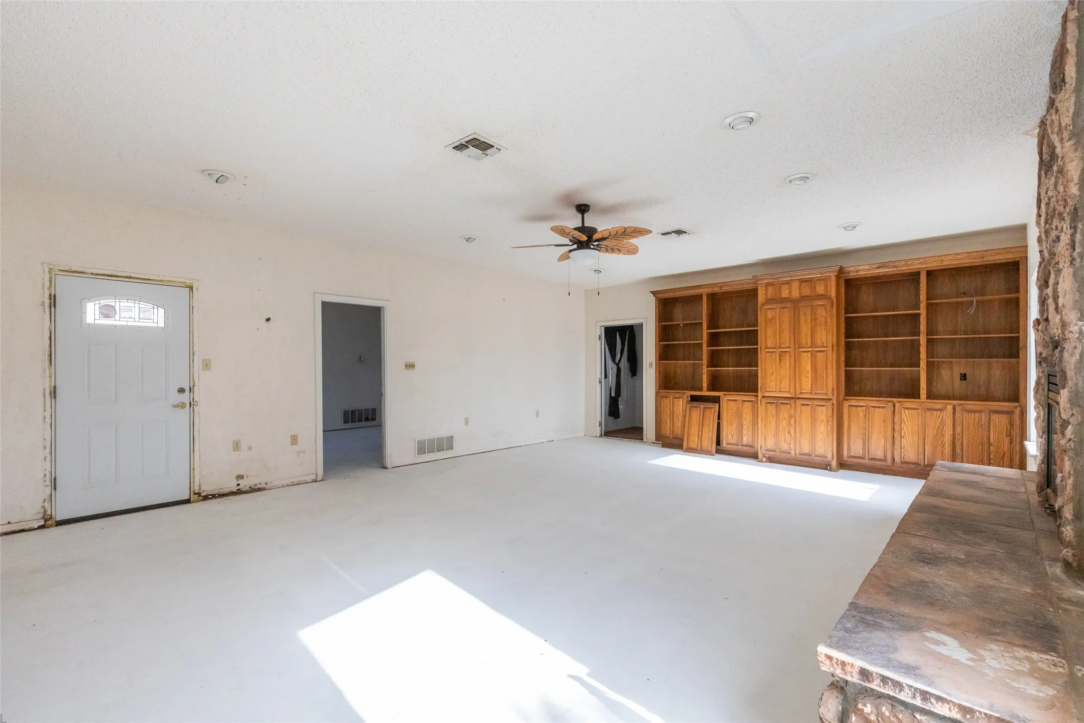 Spacious room featuring light-colored flooring, a built-in wooden shelving unit, recessed lighting, and a ceiling fan