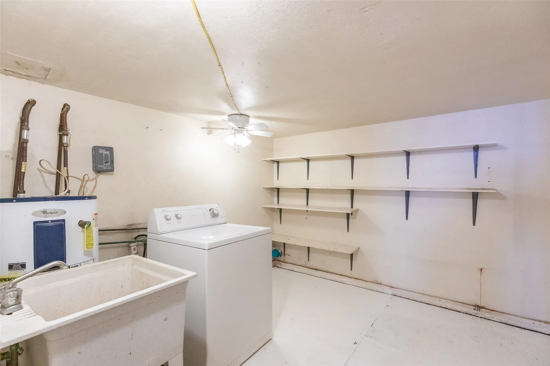 Utility room featuring a built-in utility sink, installed water heater, ceiling fan, and extensive wall-mounted shelving
