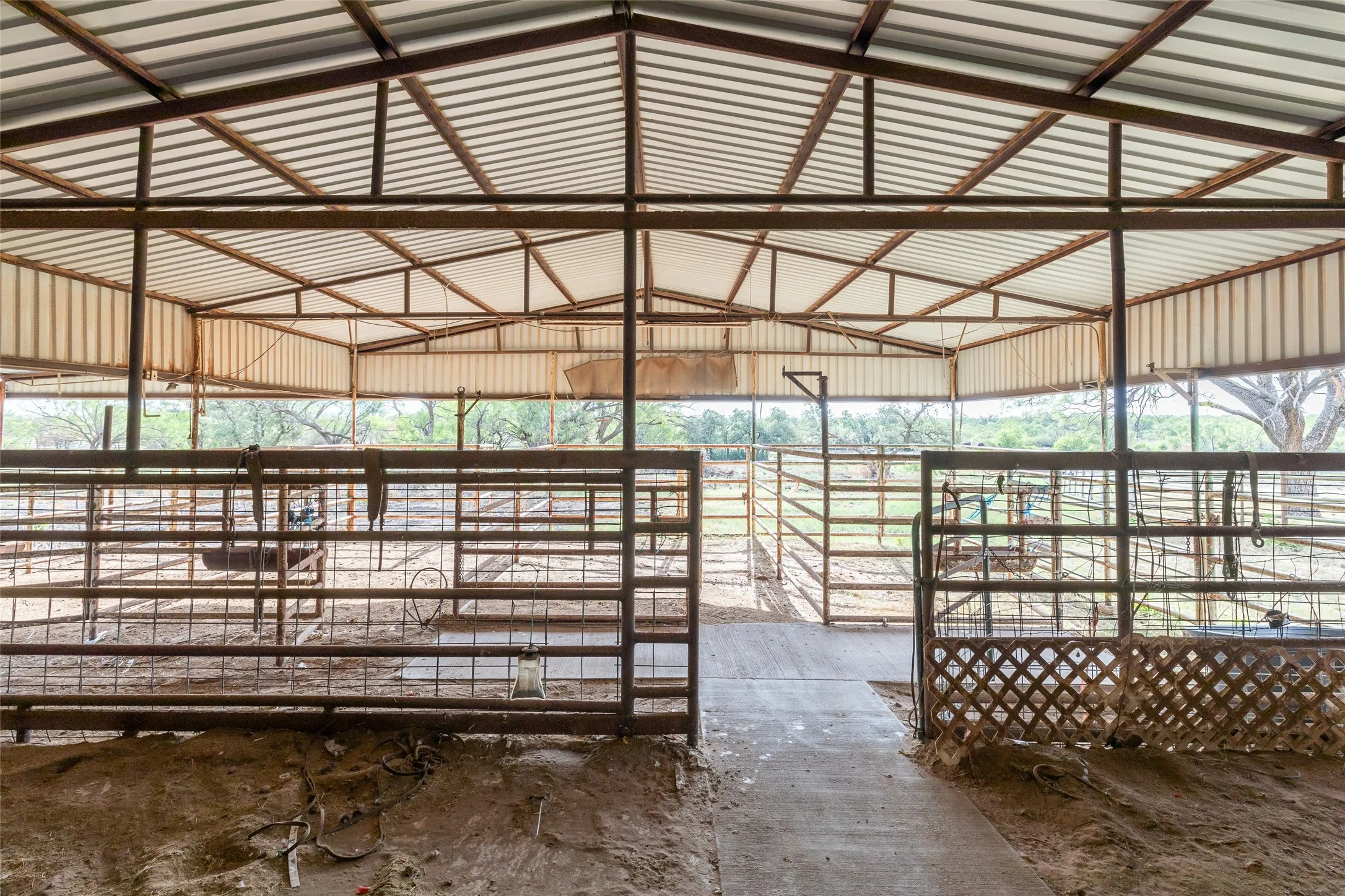 Covered metal structure featuring a corrugated roof, open-air design, and multiple metal corrals