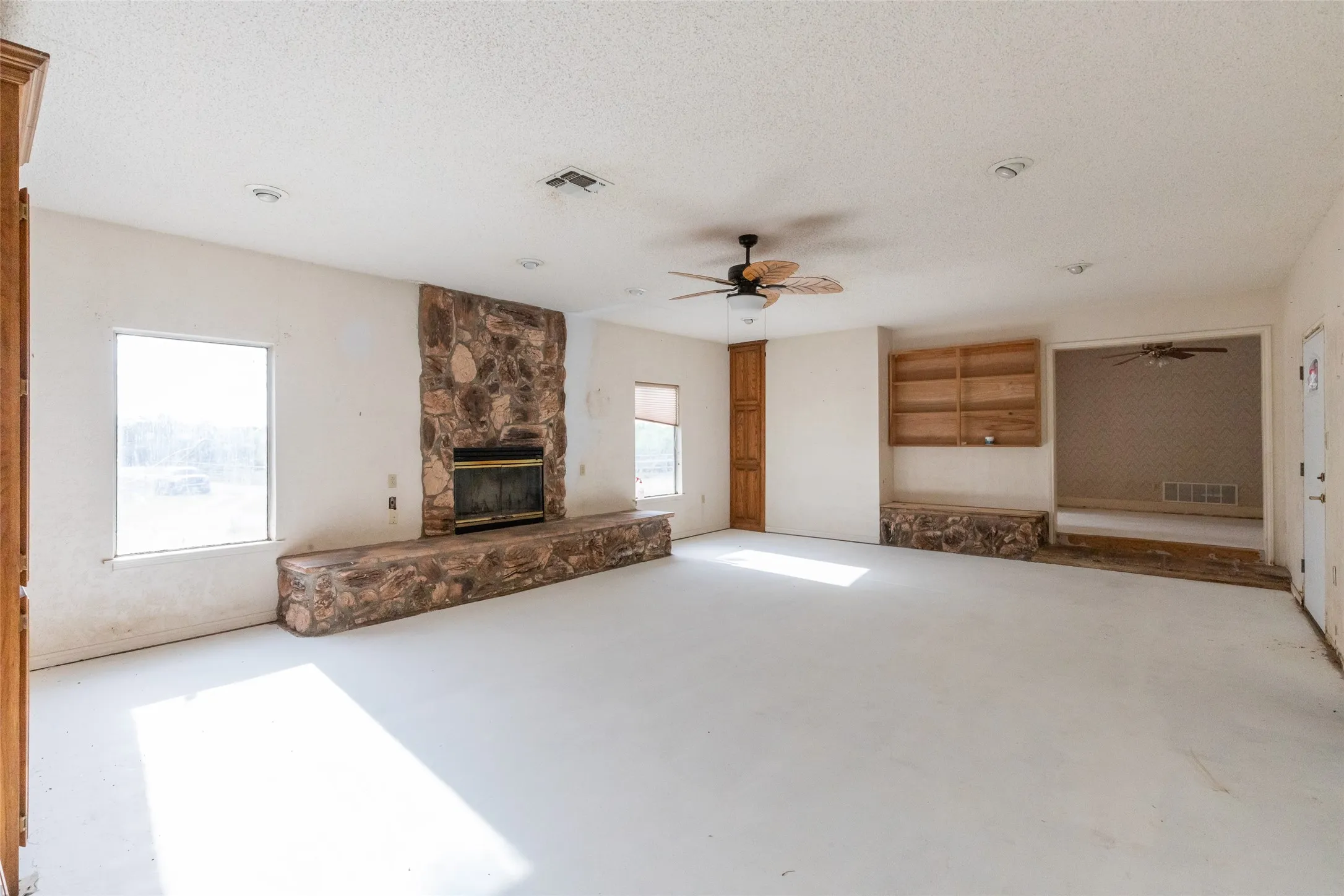 Spacious interior featuring a stone-clad fireplace with hearth, multiple windows, built-in wooden shelving, and a ceiling fan