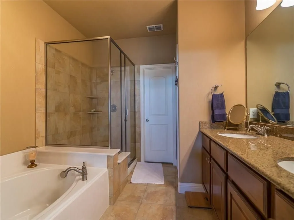 Spacious bathroom featuring a built-in soaking tub, a separate glass-enclosed shower with tiled walls, and a dual vanity with a stone countertop and integrated sinks