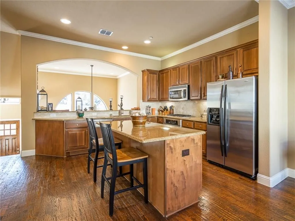 Kitchen featuring wood cabinetry, stainless steel appliances, a center island with bar seating, and granite countertops