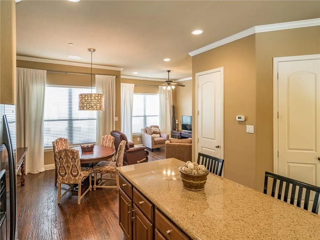 Open-concept living area featuring rich wood-finish flooring, a kitchen island with a speckled countertop, a dining area with an overhead decorative pendant light, and a living room with a ceiling fan