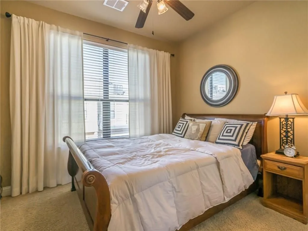 Bedroom featuring a large window with blinds and drapes, carpeted flooring, and a ceiling fan with integrated lighting
