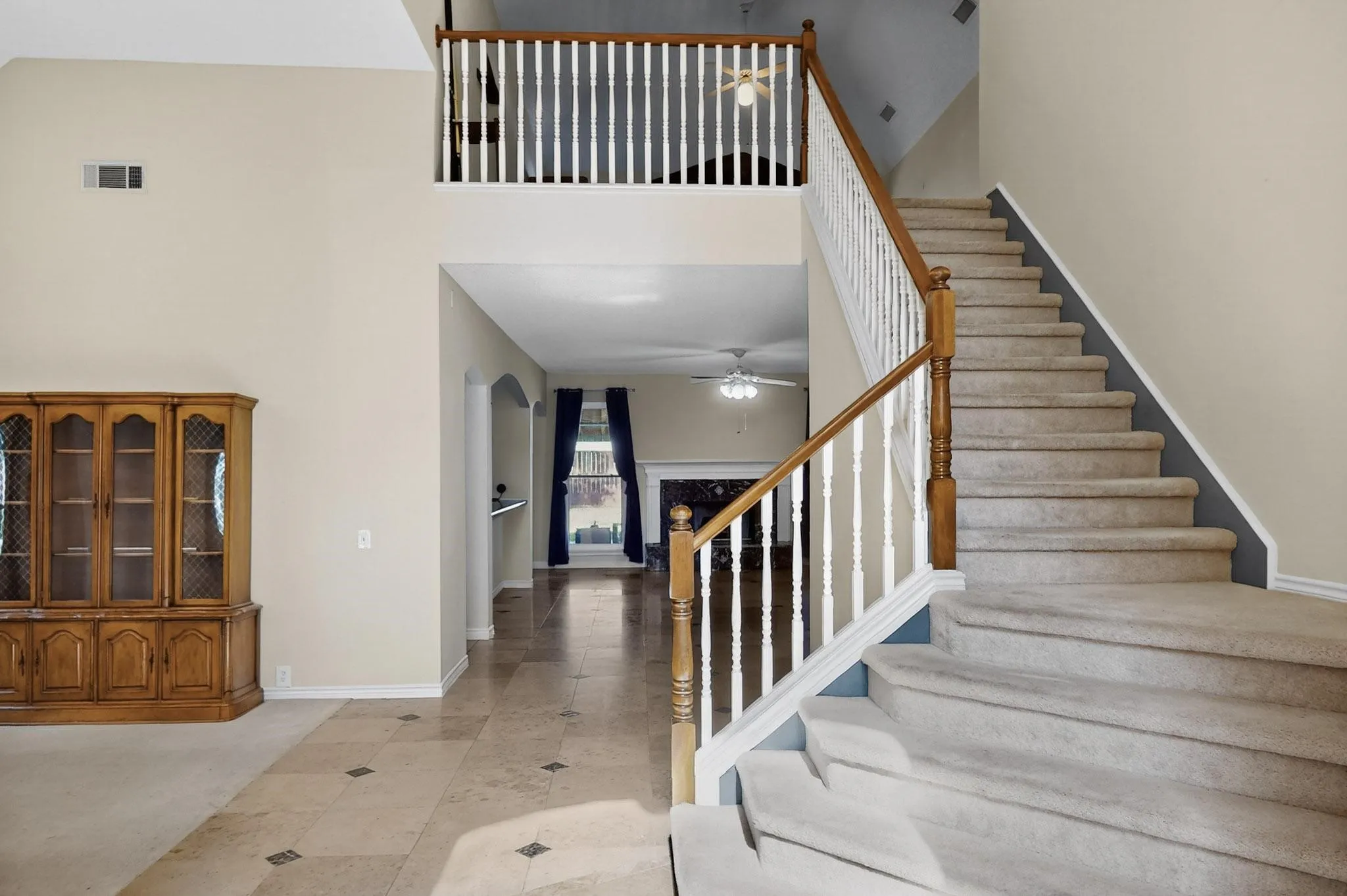 Two-story foyer featuring a carpeted staircase with wood and white baluster railing, a second-story landing with matching railing, arched doorways, and tile flooring with decorative inserts
