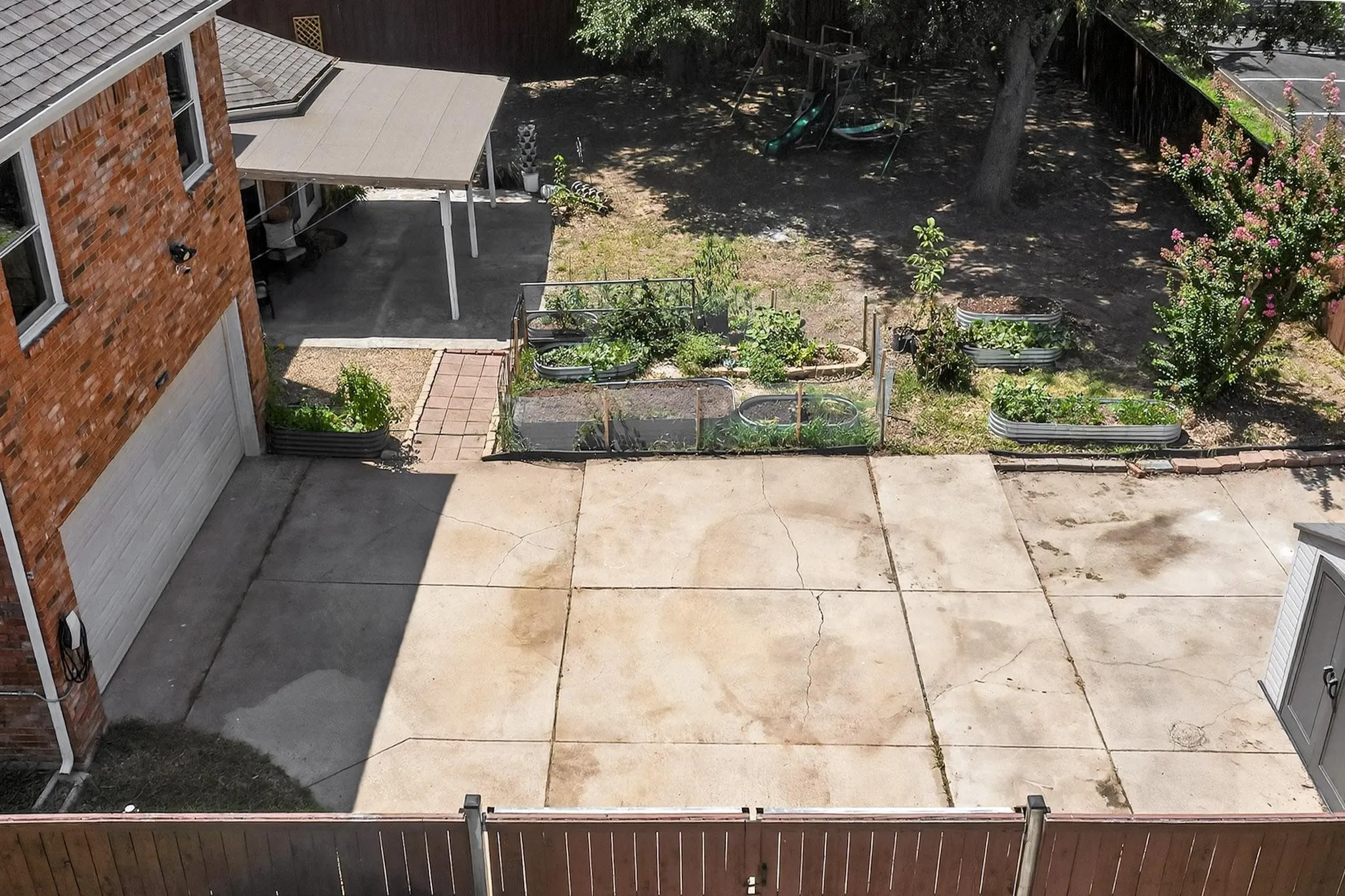 Spacious concrete patio with raised garden beds, a covered carport, and a brick exterior home