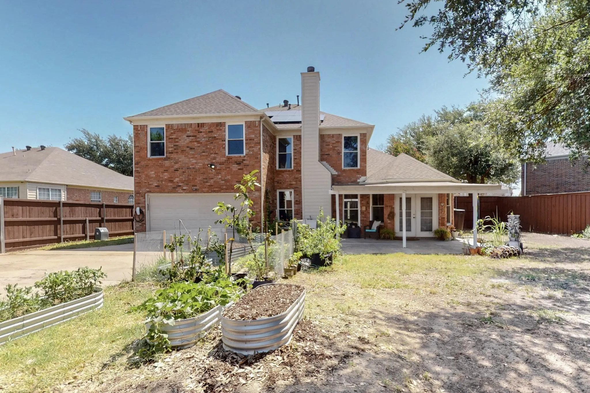 Brick exterior featuring a covered patio, dual French doors, a two-car garage, and multiple raised garden beds