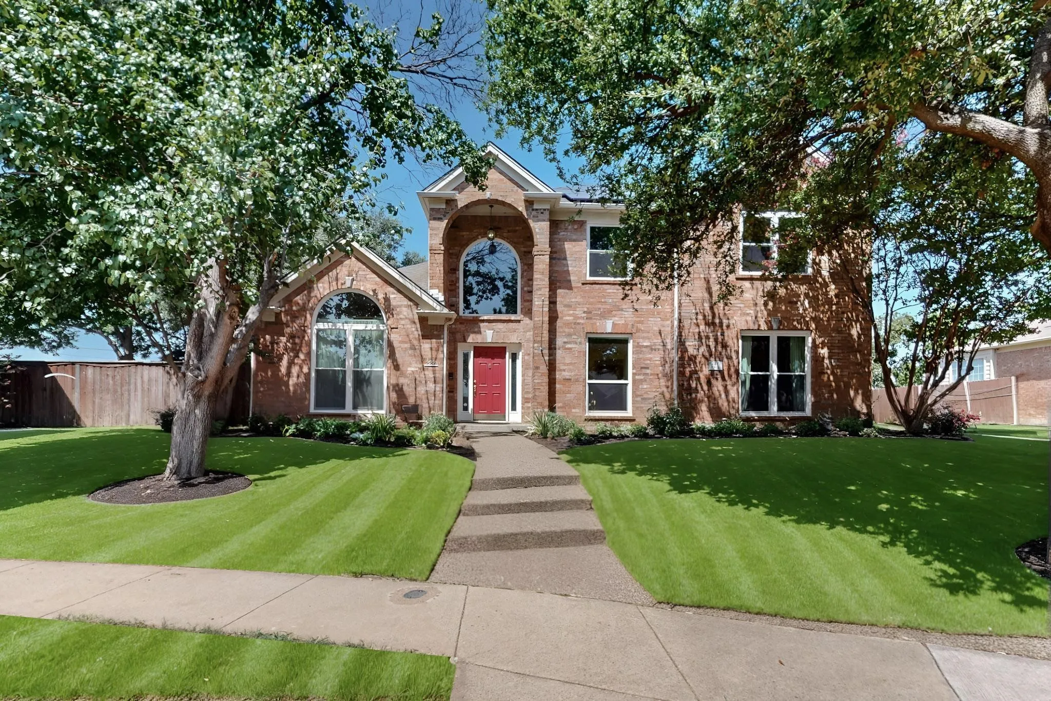 Two-story brick facade residence featuring a prominent arched window, a red entry door, a multi-pane arched window, and a concrete paver walkway
