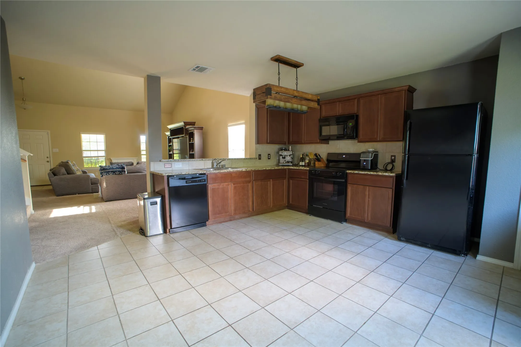Kitchen featuring tile flooring, wooden cabinetry, stone-finish countertops, and black appliances