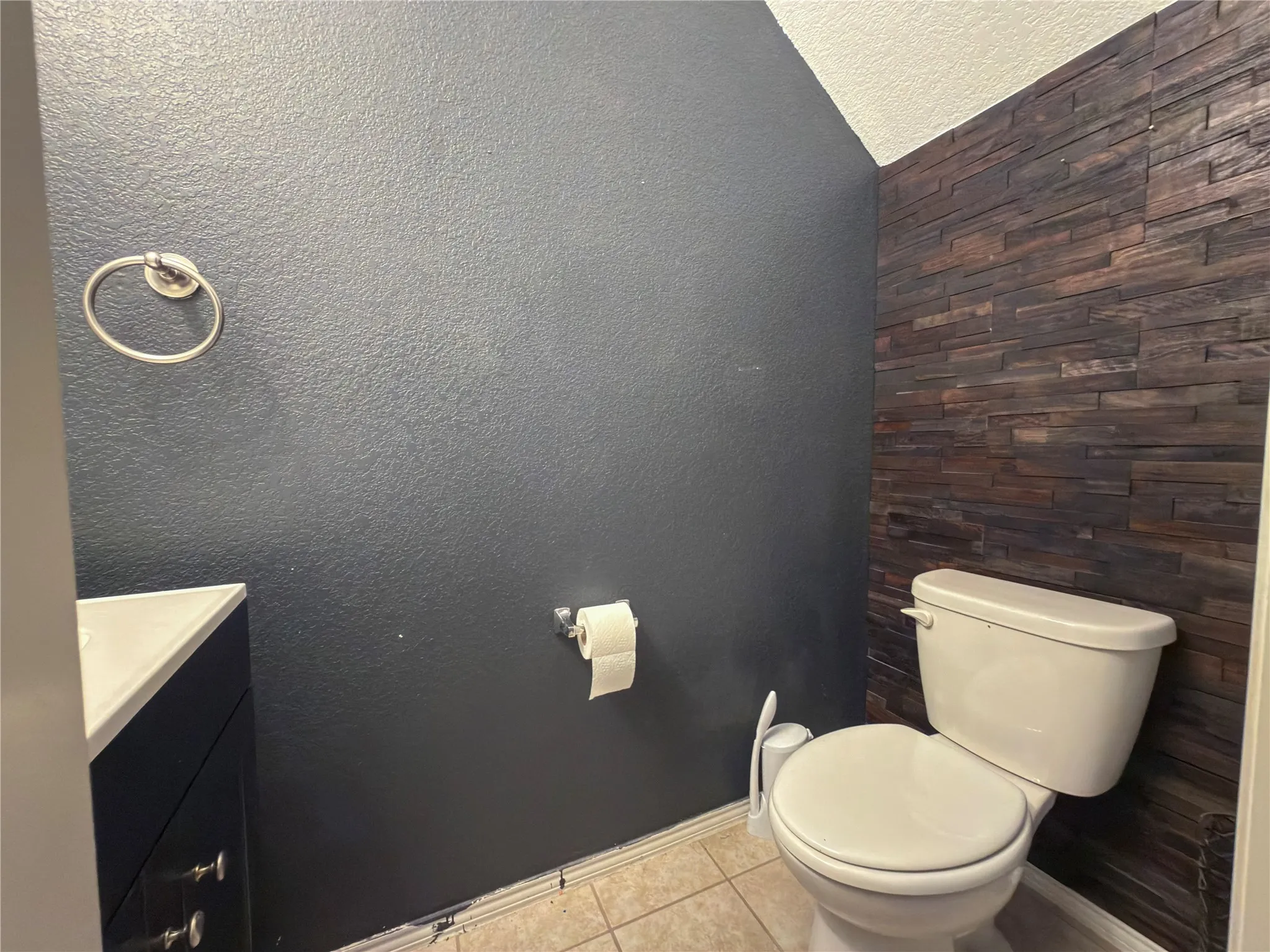 Half bath downstairs featuring a wood-finish accent wall, white toilet, and dark cabinetry with a light-colored countertop