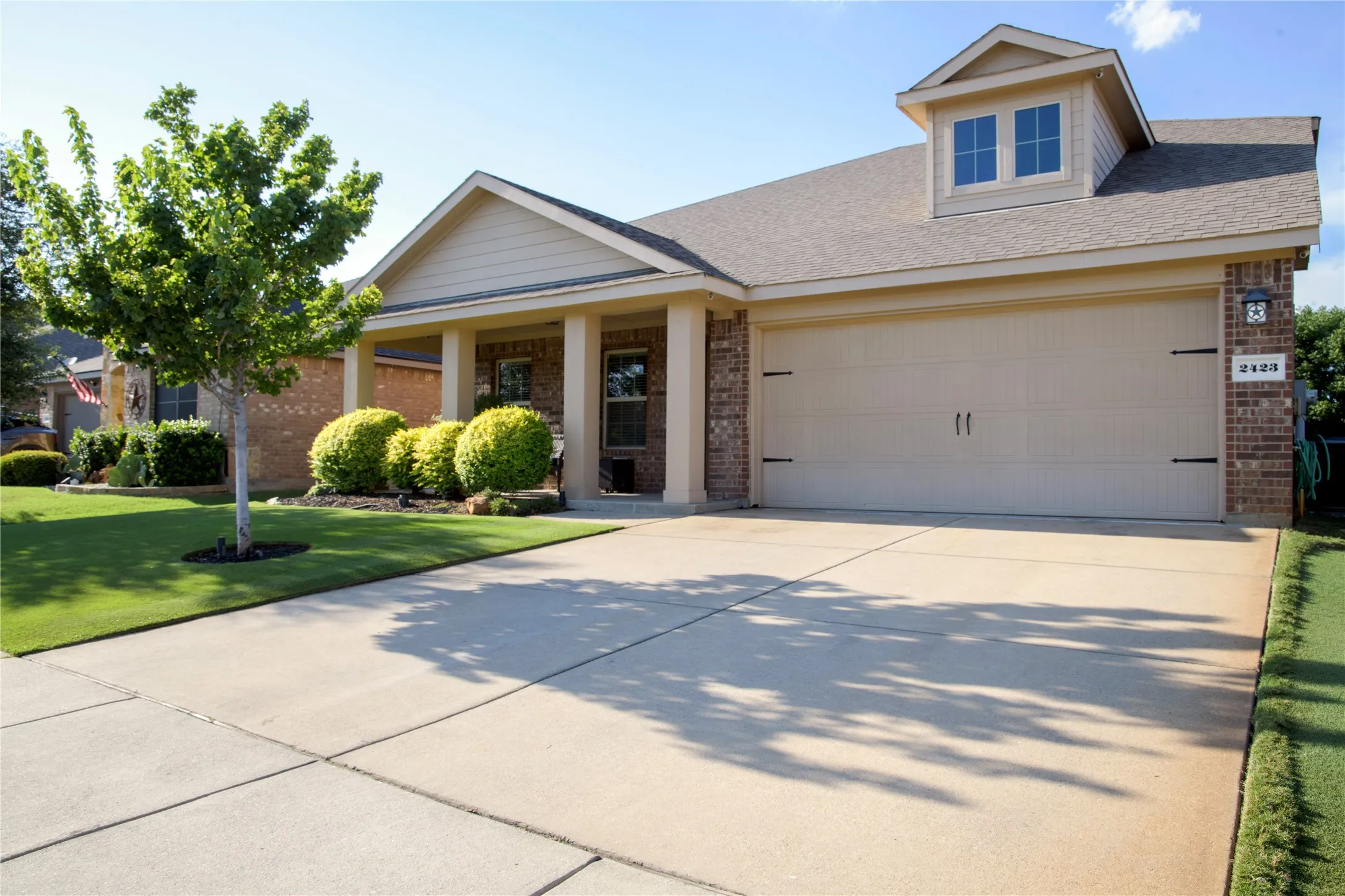 Single-story residence featuring a two-car garage with decorative hardware, a covered entry porch with columns, brick and siding exterior finishes, a dormer window, and a concrete driveway