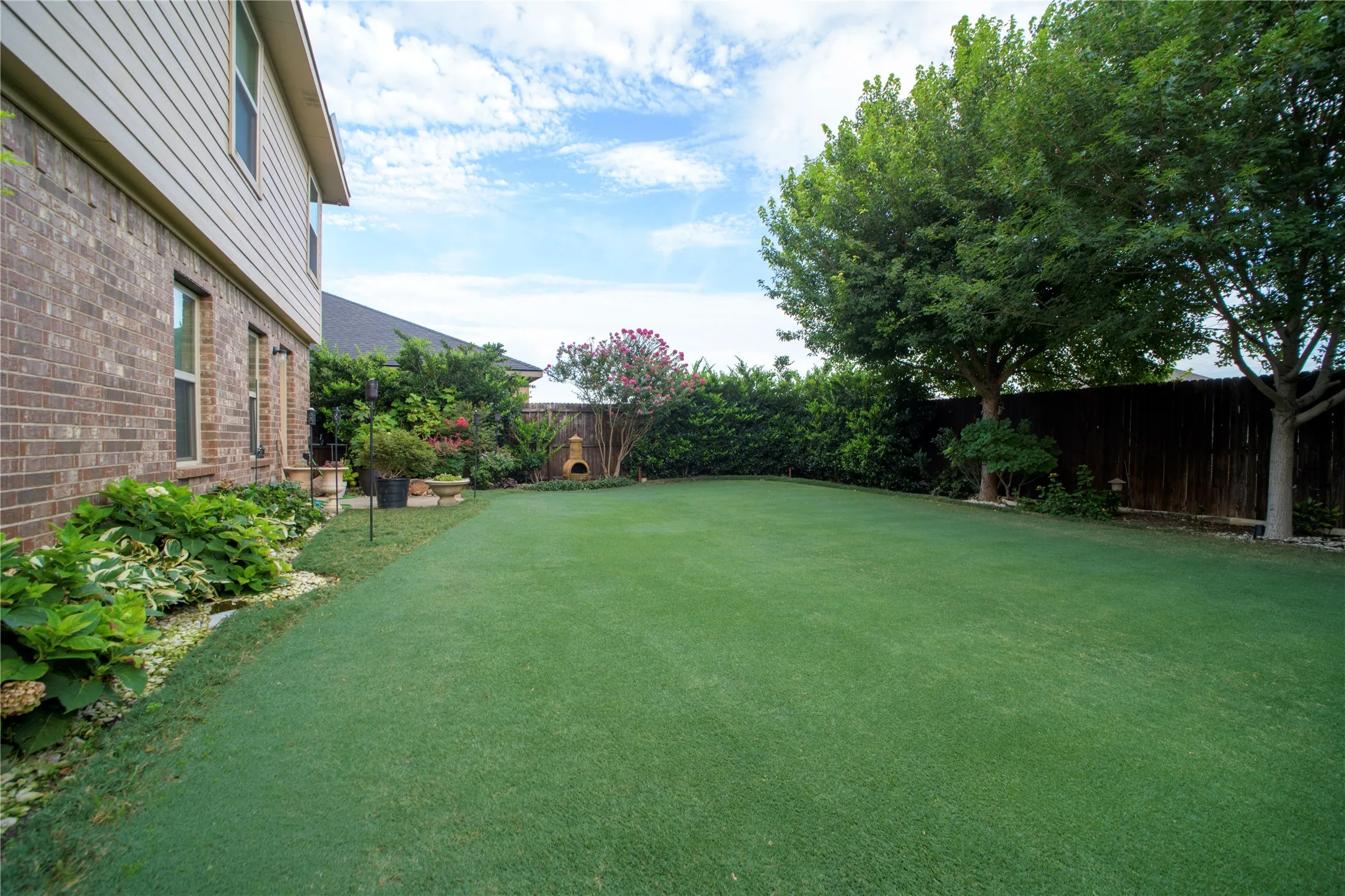 Expansive green lawn with a mature tree backdrop and perimeter landscaping