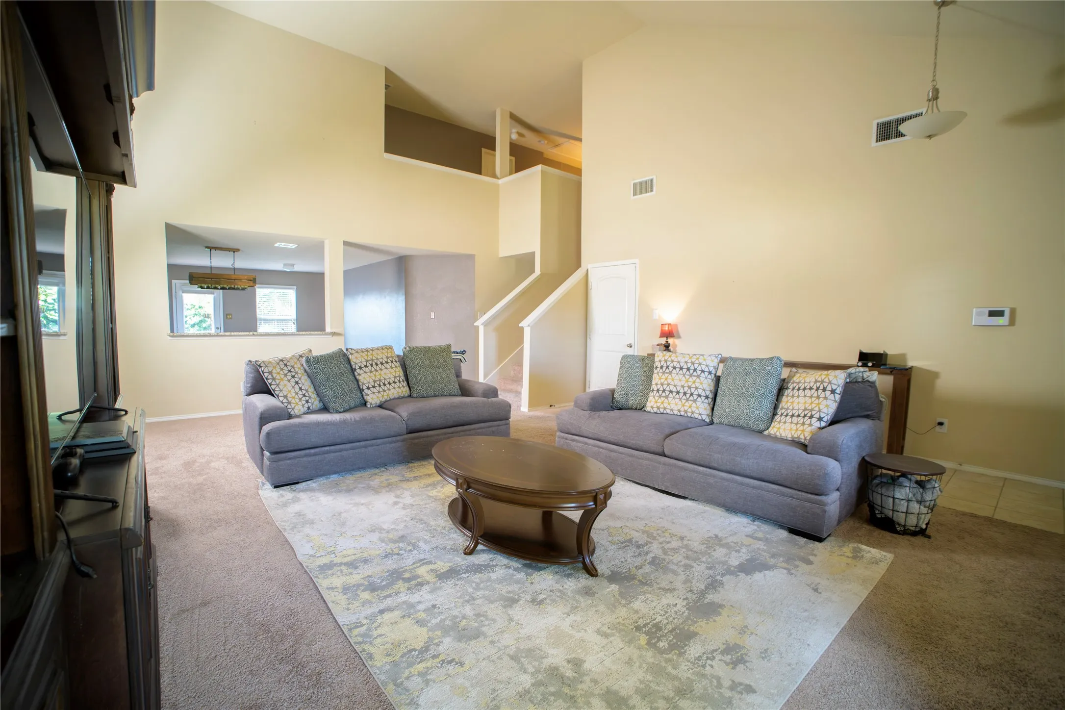 Open concept living area featuring vaulted ceilings, carpet flooring, a pass-through window, and a staircase with white railings