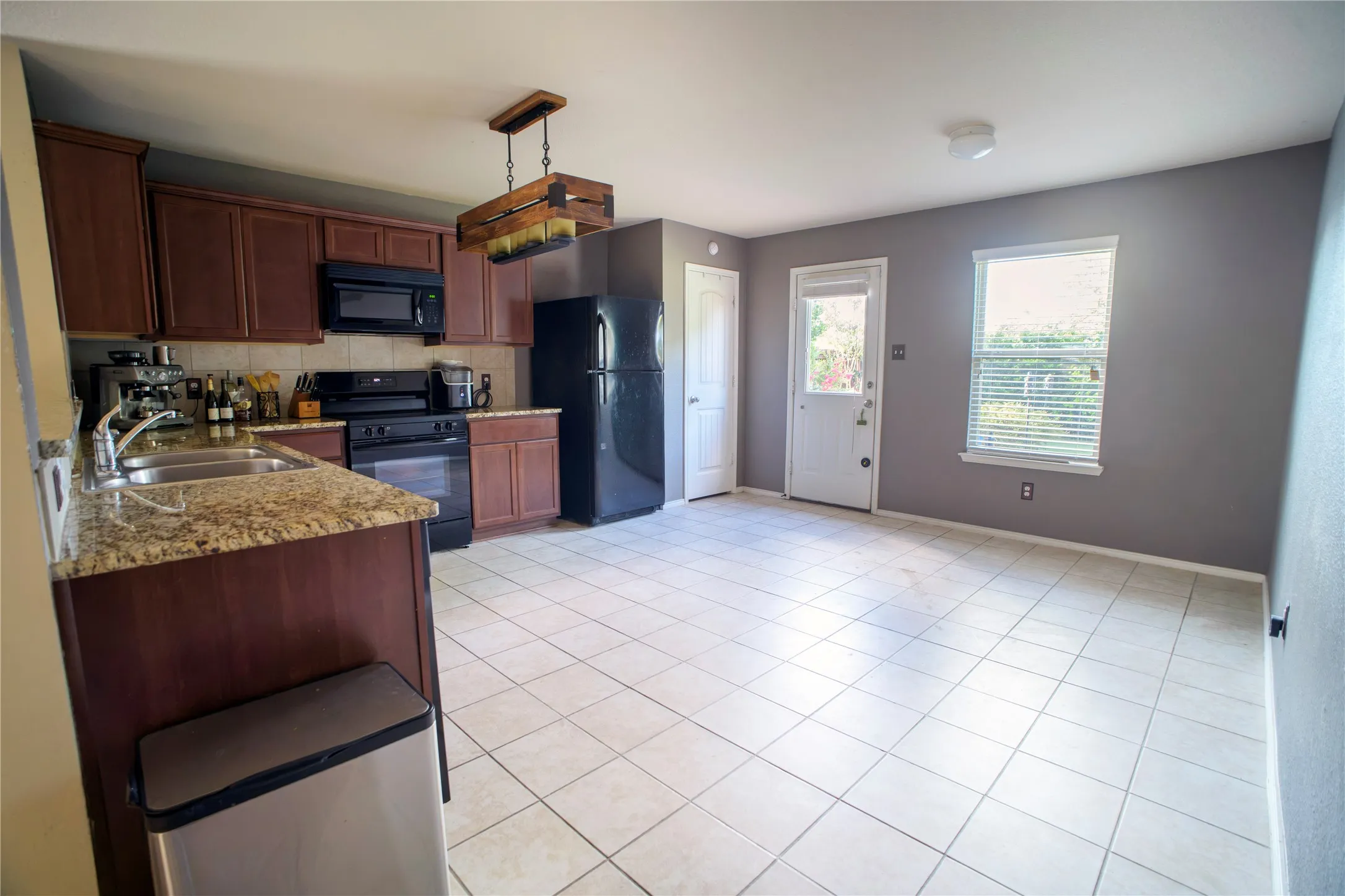Kitchen featuring rich wood cabinetry, granite-finish countertops, and black appliances including an oven and microwave