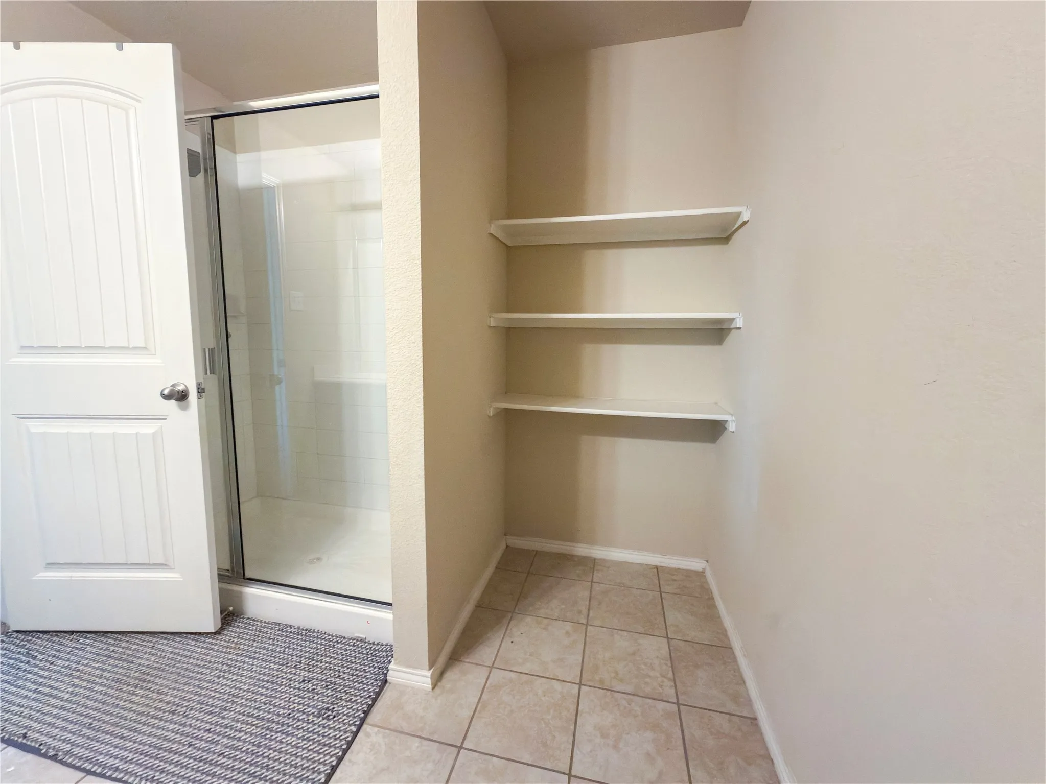 Walk-in shower with clear glass enclosure and tile surround, alongside built-in shelving and tile flooring
