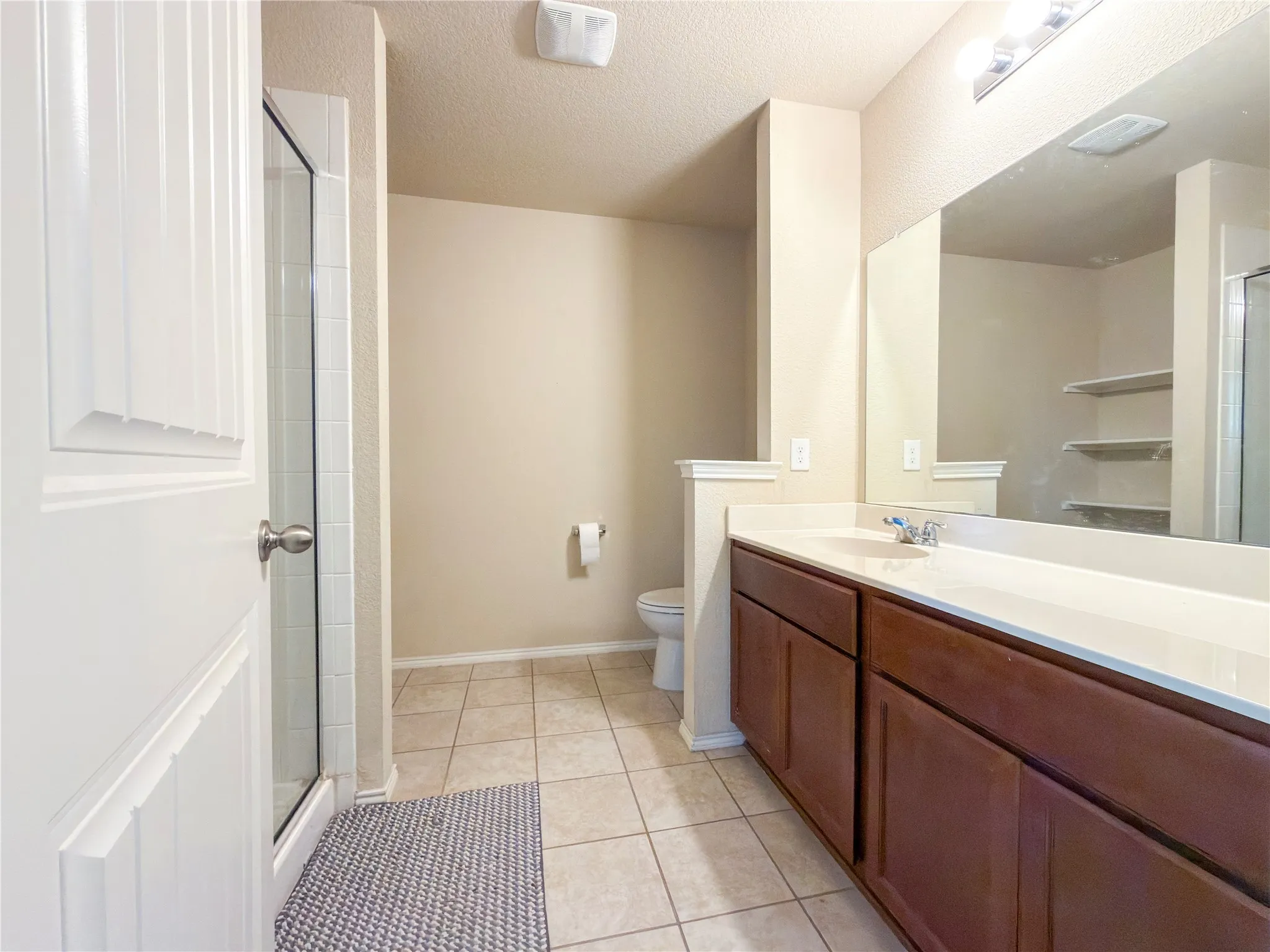 Bathroom featuring a double vanity with dark wood-finish cabinetry, a large integrated mirror, and a glass-enclosed shower