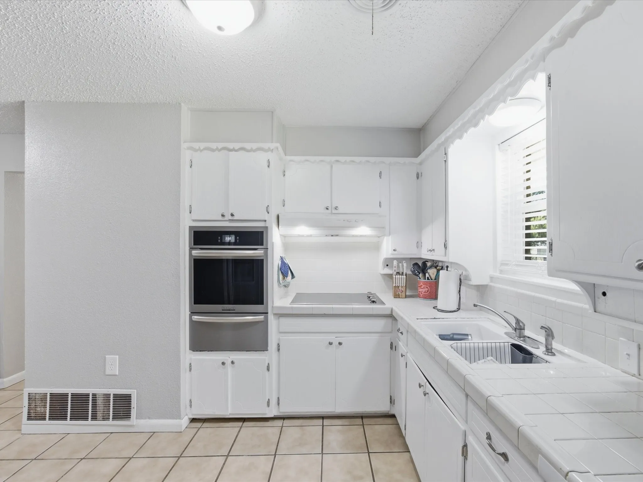 Kitchen featuring white cabinetry, Stainless steel oven, tile countertops, and tile flooring