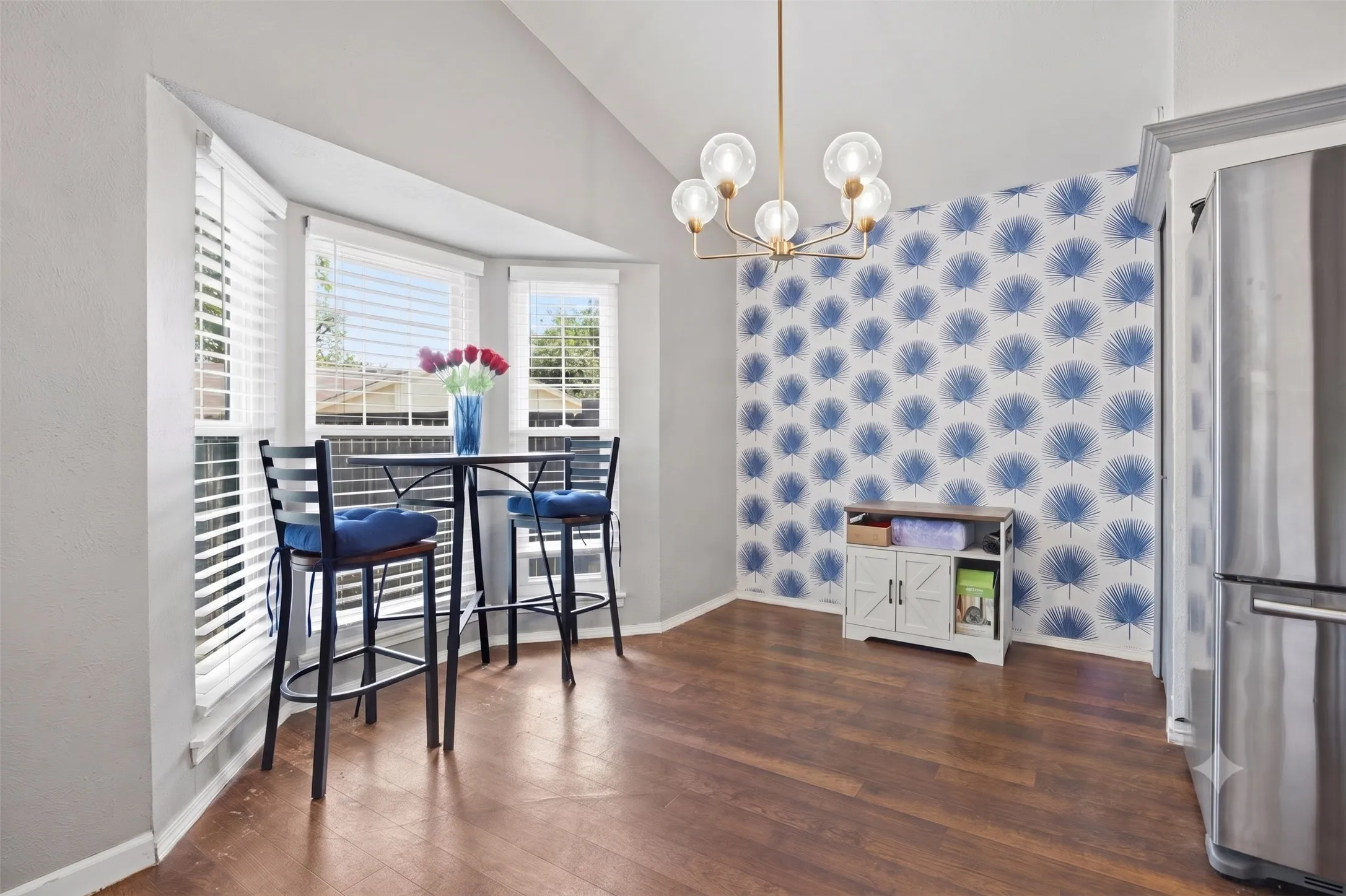 Sunny breakfast nook off the kitchen, framed by a bay
window and a bold botanical wallpaper wall.