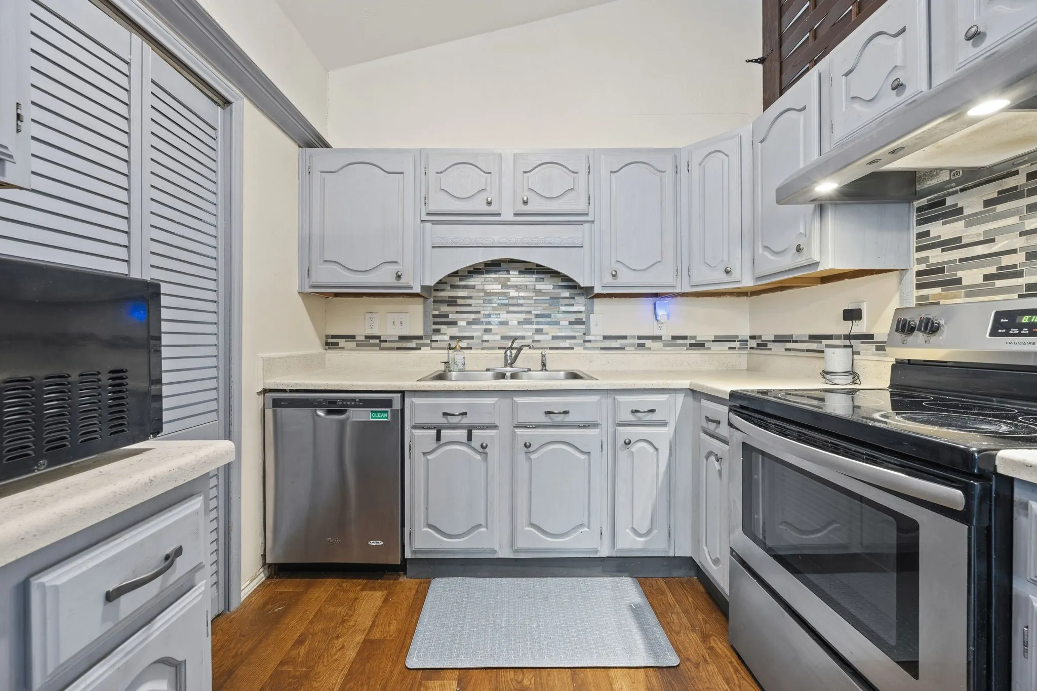 Kitchen featuring soft gray cabinetry, a mosaic tile
backsplash, and stainless dishwasher and range