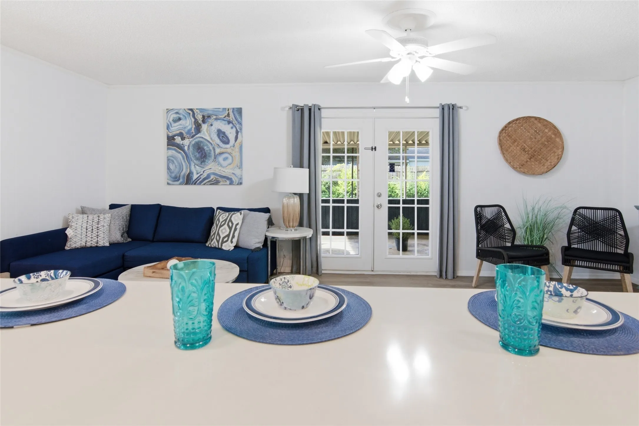 Open-concept living area with light-toned flooring, featuring a pair of French doors, a ceiling fan, and white walls
