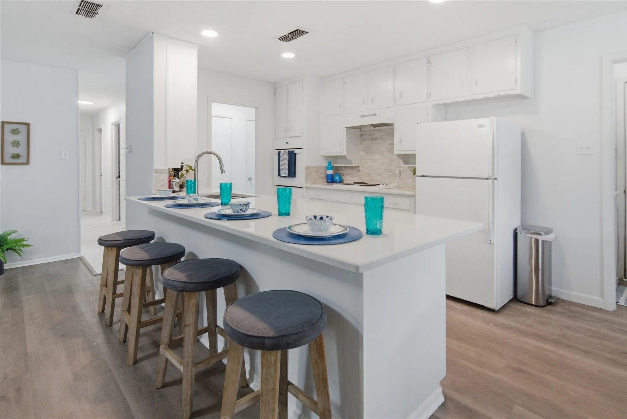 Contemporary kitchen featuring white cabinetry, a large kitchen island with counter seating, a stainless steel faucet, and wood-finish flooring