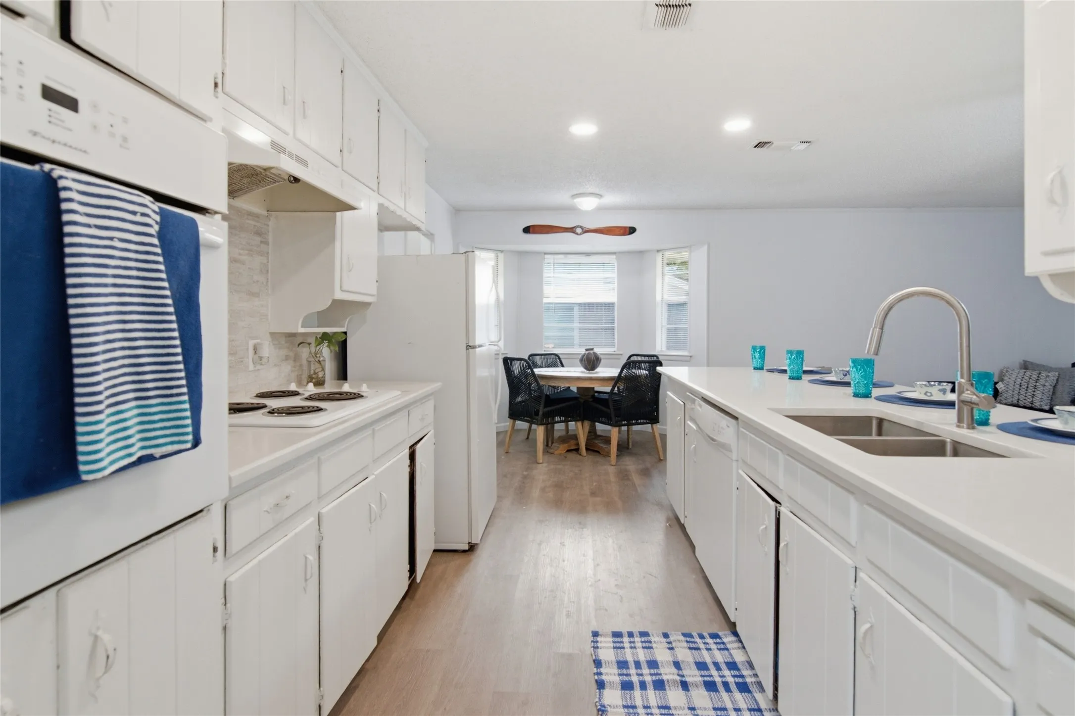 Galley kitchen featuring wood-finish flooring, white cabinetry, integrated oven, and a double basin sink with a gooseneck faucet
