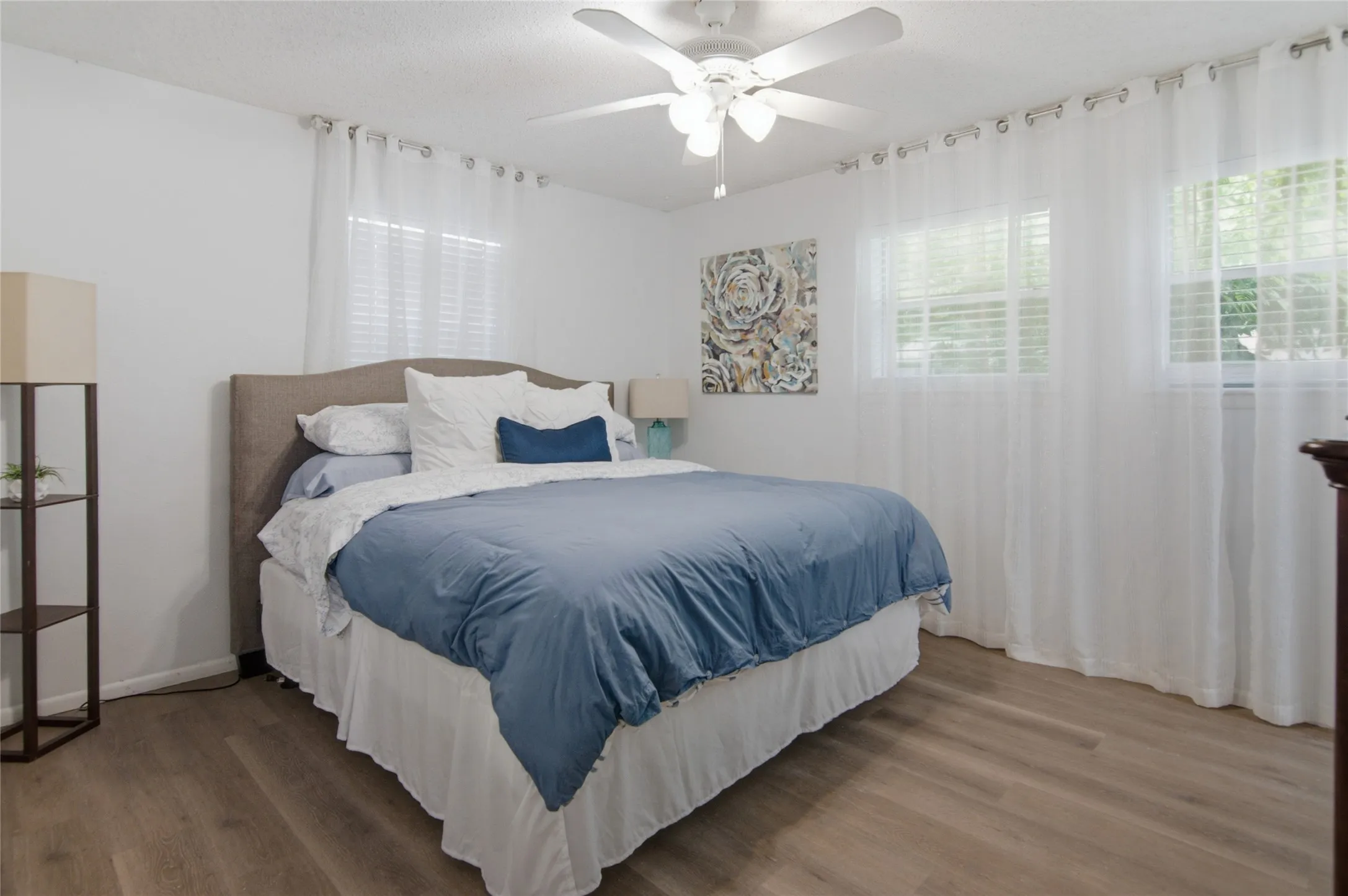 Spacious room featuring wood-finish flooring, multiple windows, a ceiling fan, and white walls