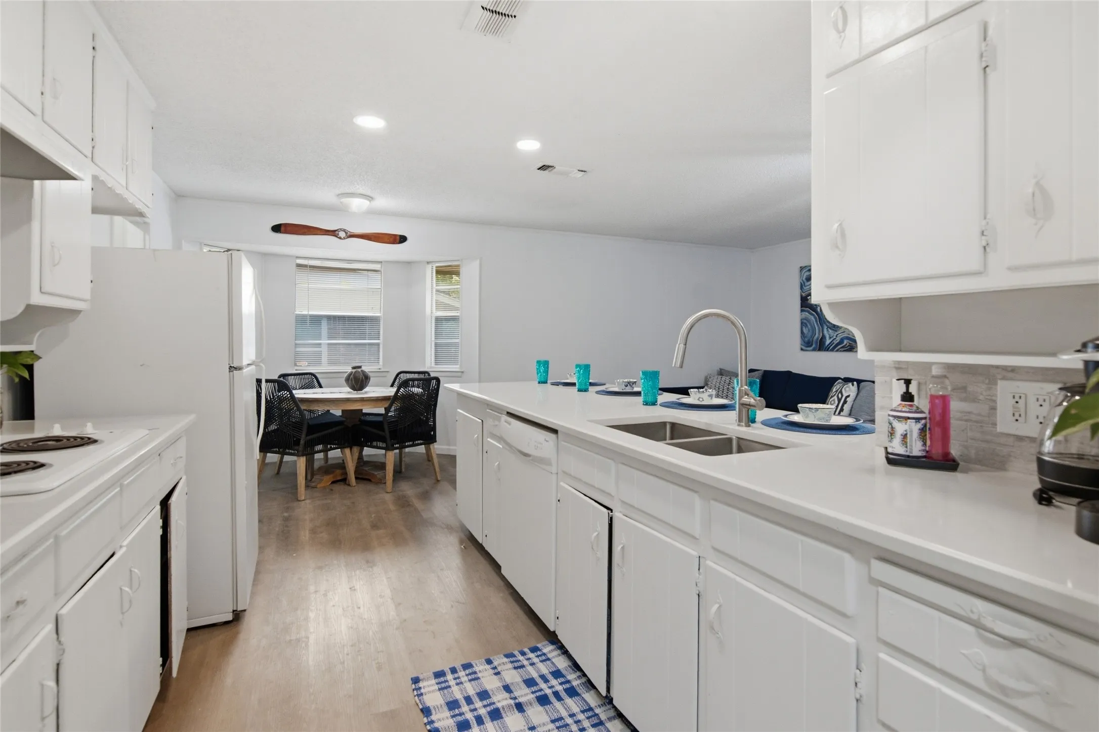 Kitchen featuring white cabinetry, light-toned countertops, a double basin stainless steel sink, and wood-finish flooring