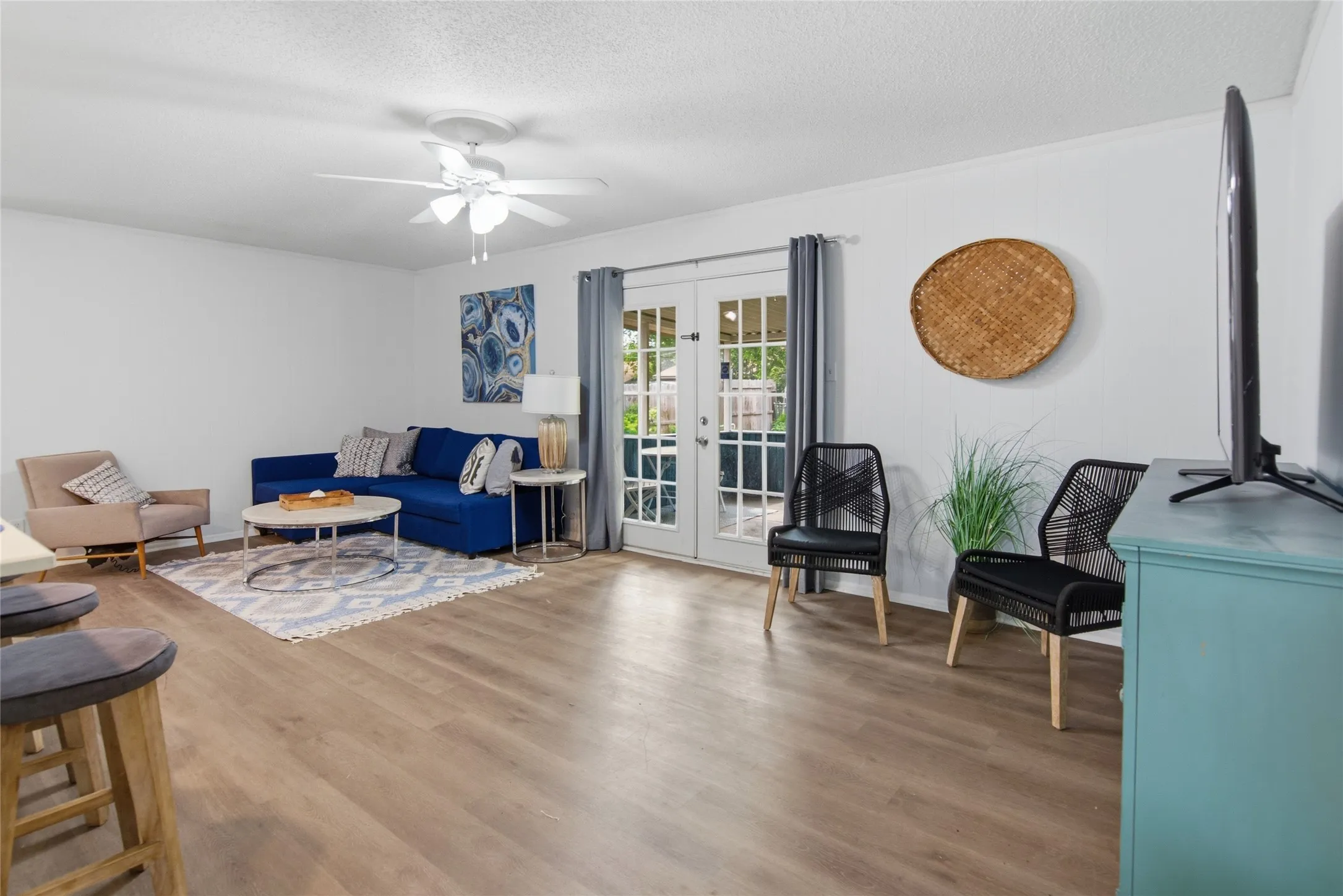 Spacious living area featuring wood-finish flooring, white walls, and a ceiling fan with integrated lighting