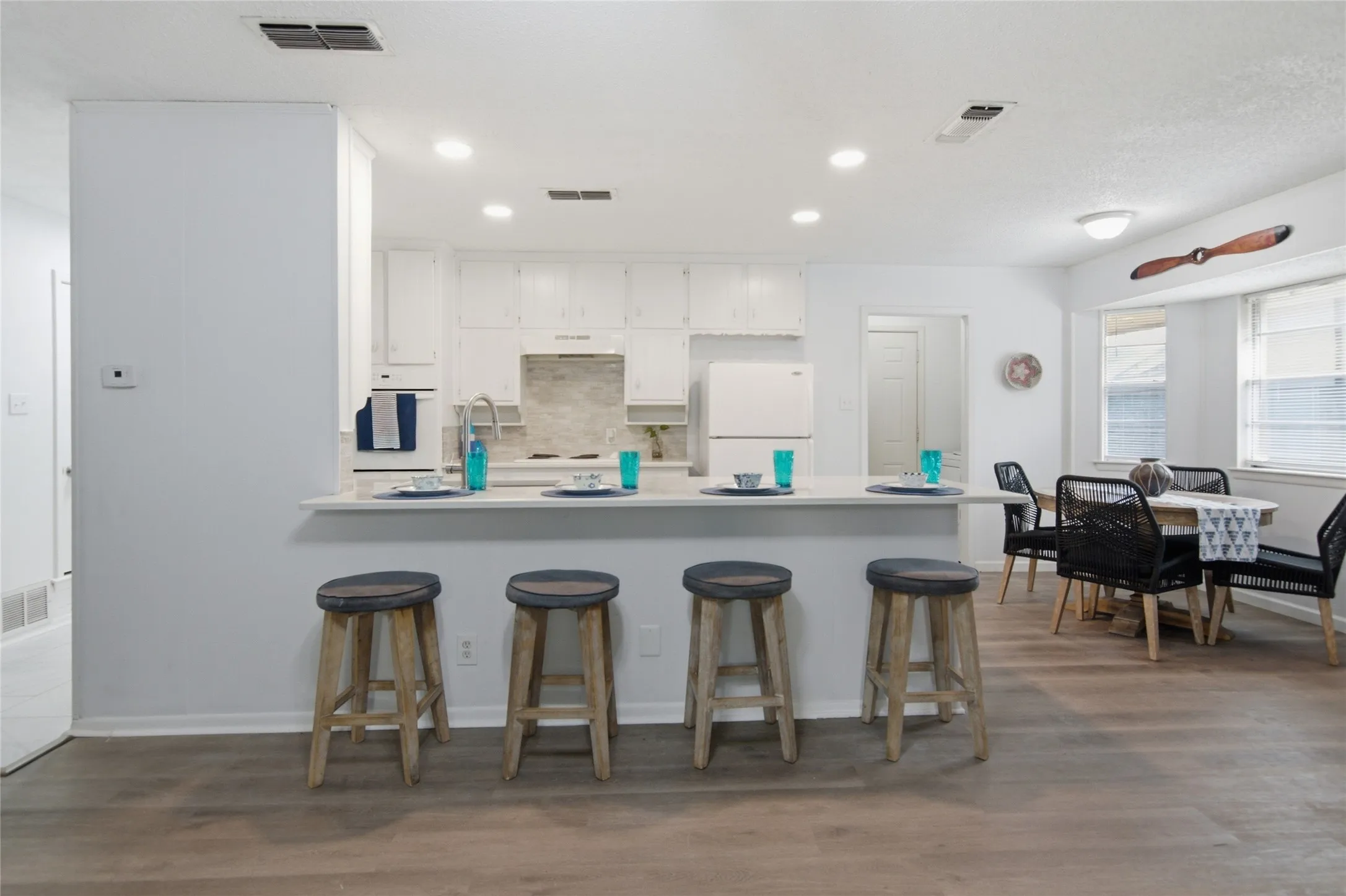 Open-concept kitchen and dining area featuring a breakfast bar with seating, white cabinetry, light-colored countertops, and wood-finish​​‌​​​​‌​​‌‌​‌‌​​​‌‌​‌​‌​‌​​​‌​​ flooring