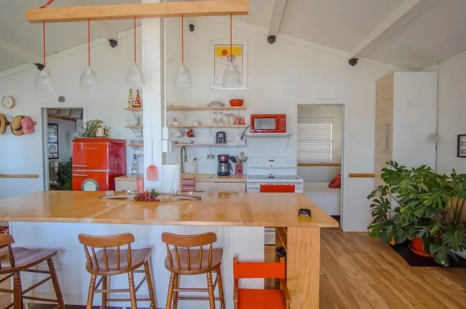Open-concept kitchen featuring vaulted ceilings with exposed beams, wood-finish flooring, a large island with seating, and open shelving