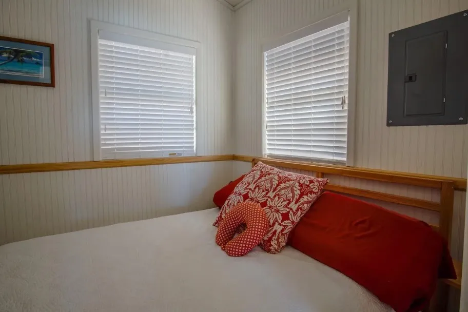 Room featuring two windows with white horizontal blinds, vertical paneling on walls, a wooden chair rail, and a wall-mounted electrical panel