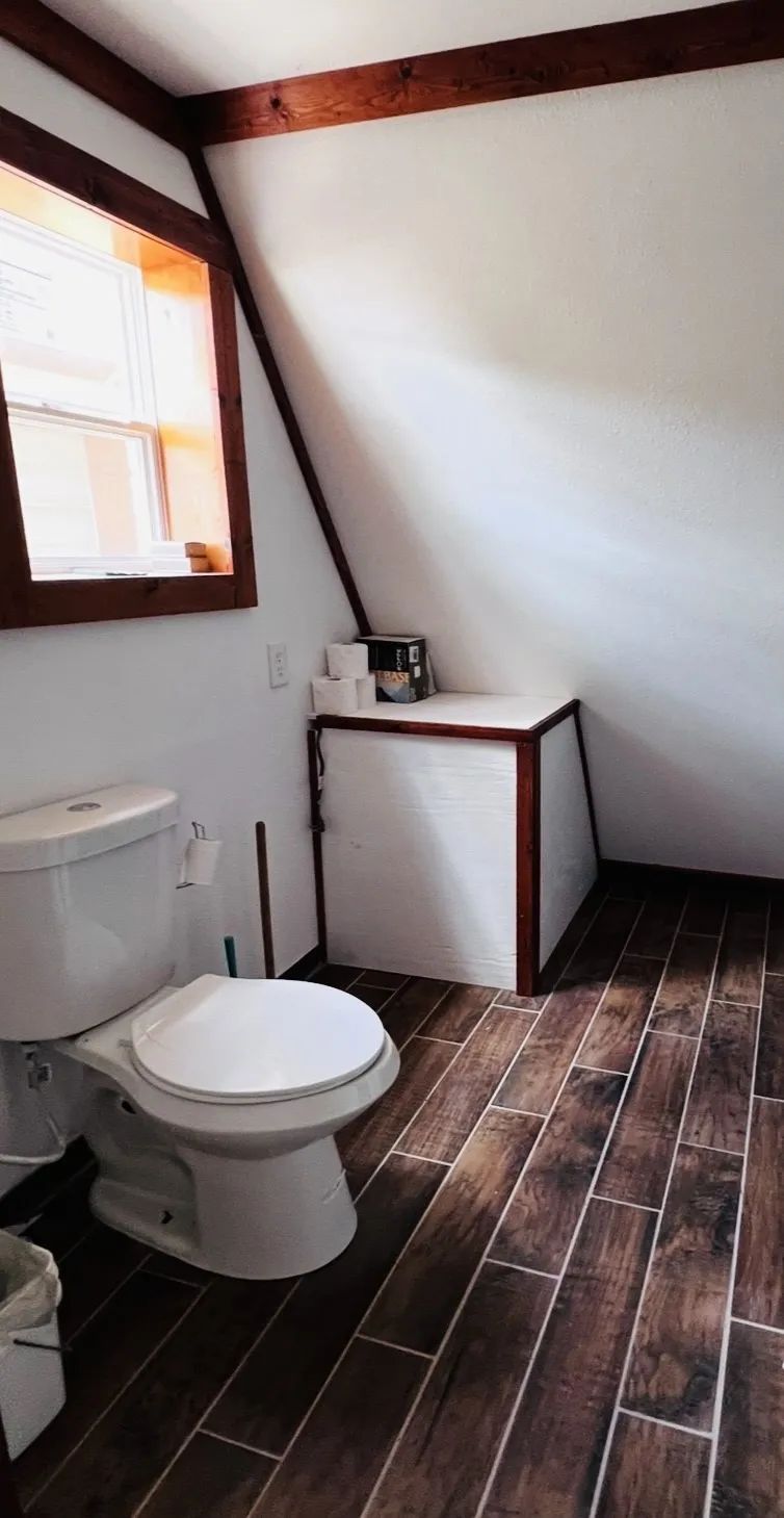 Bathroom featuring wood-finish tile flooring, a white porcelain toilet, and a built-in storage unit