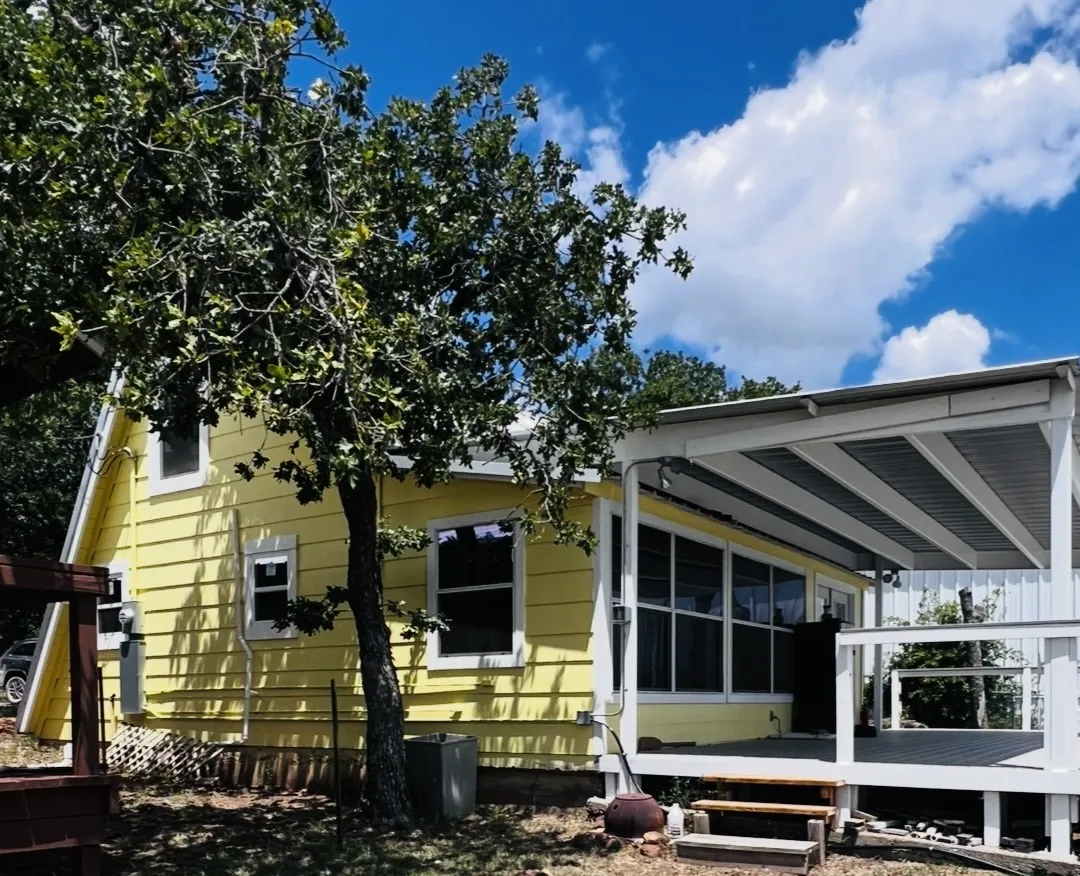 Yellow siding exterior with white trim, featuring a covered deck with a white railing and corrugated metal roof