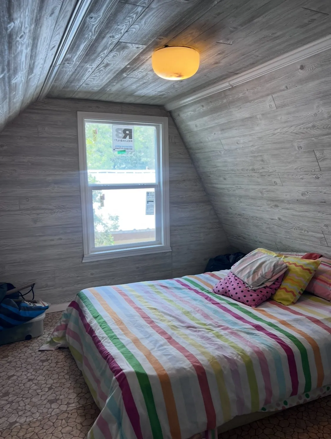 Attic space featuring sloped wood-finish paneling, a ceiling-mounted light fixture, and a white-framed window