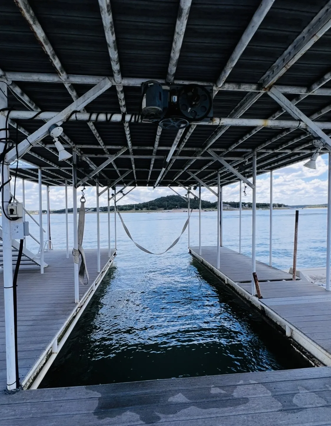 Boat dock with composite decking, featuring a covered boat slip, boat lift, and overhead lighting fixtures