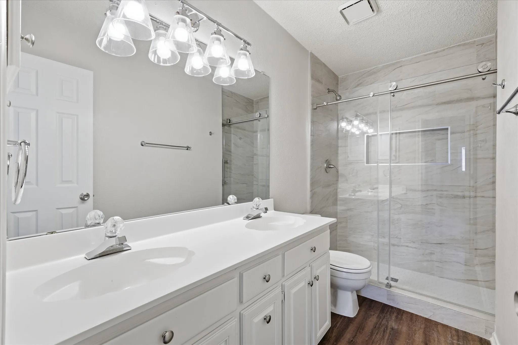 A beautifully updated bath showcases dual sinks and a striking walk-in shower with floor-to-ceiling tile and frameless glass.