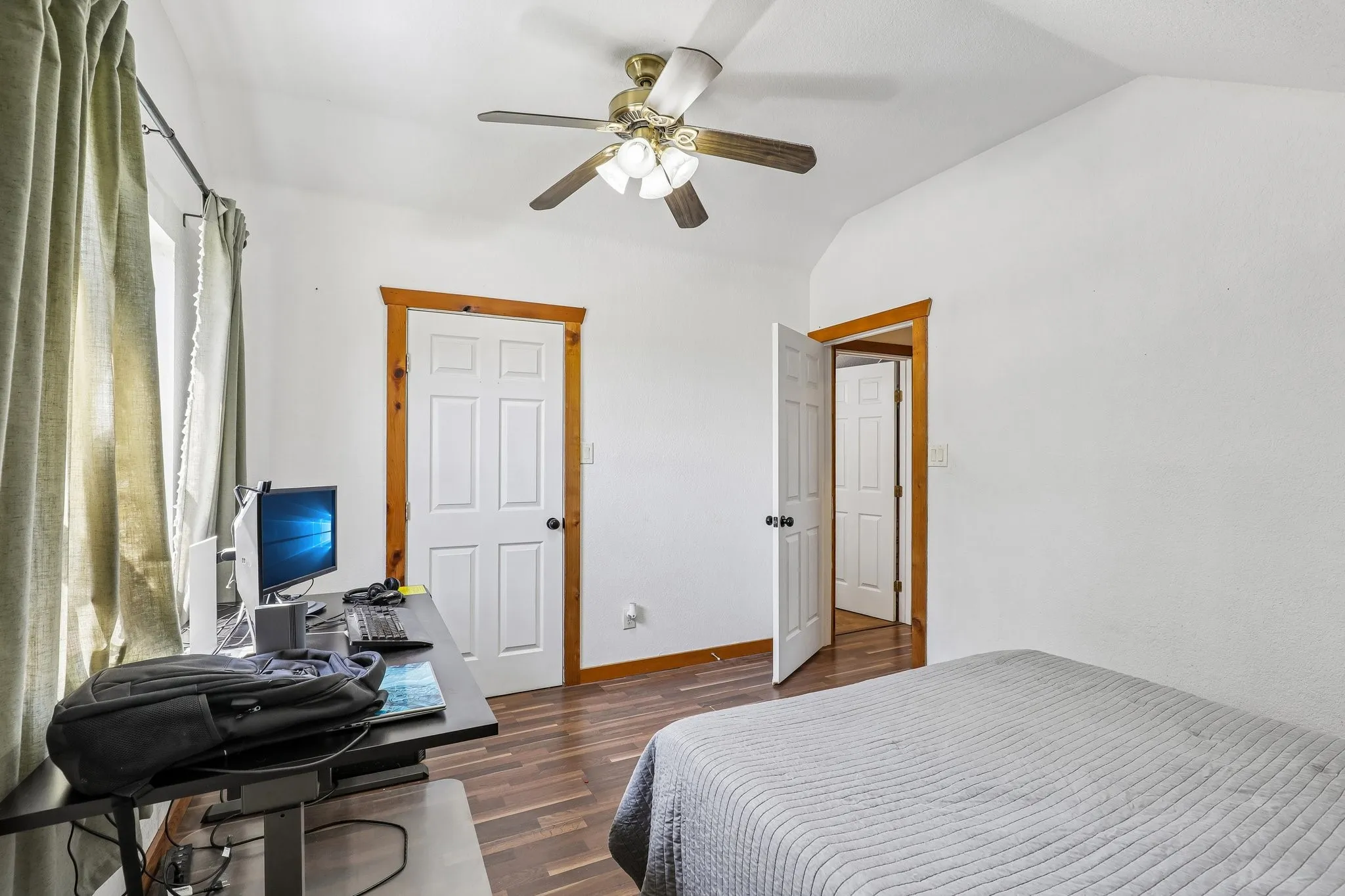 Room featuring wood-finish flooring, white paneled doors with natural wood trim, and a ceiling fan with integrated lighting
