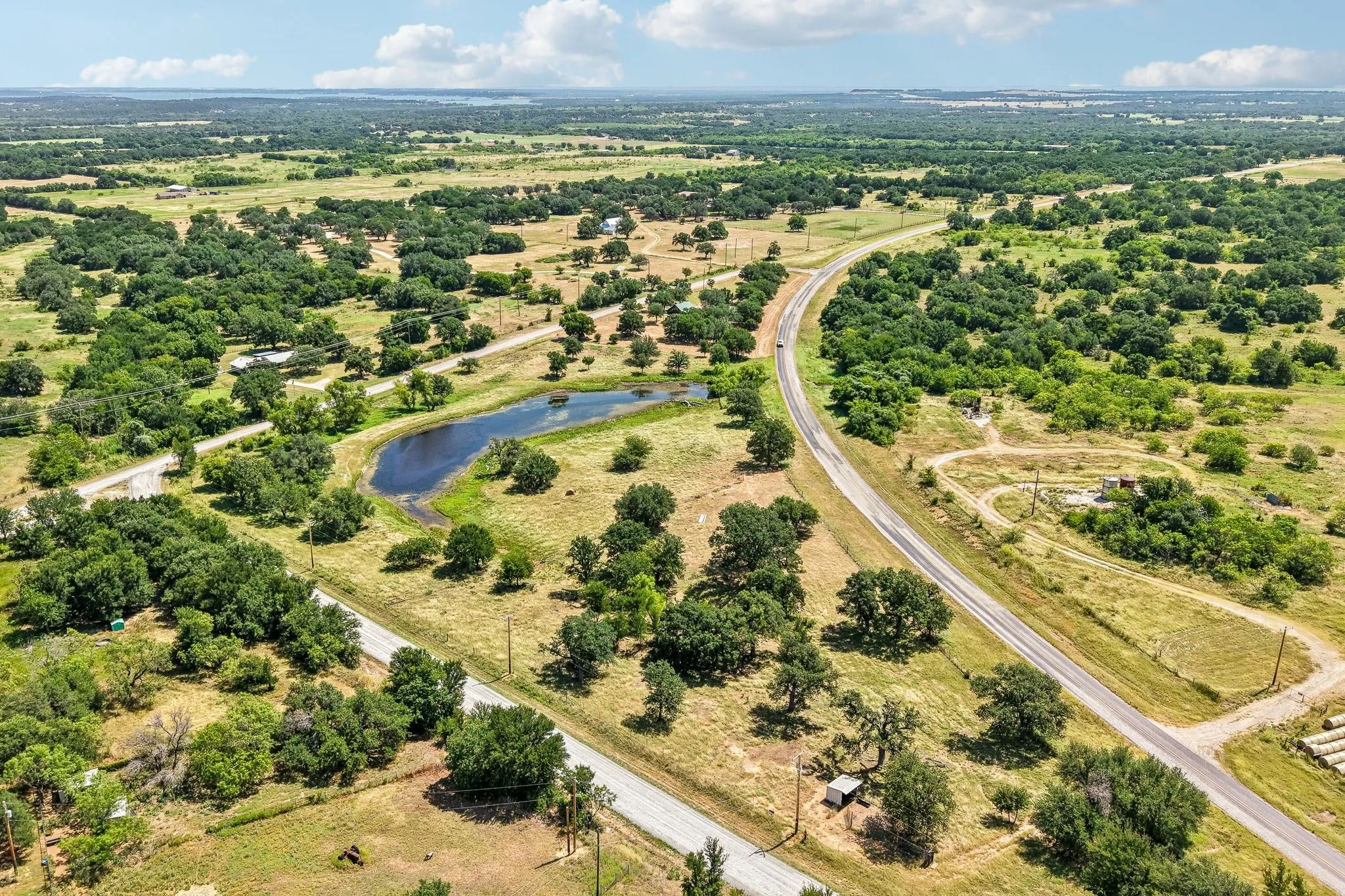 Expansive rural landscape featuring a private pond, mature trees, and a winding paved road