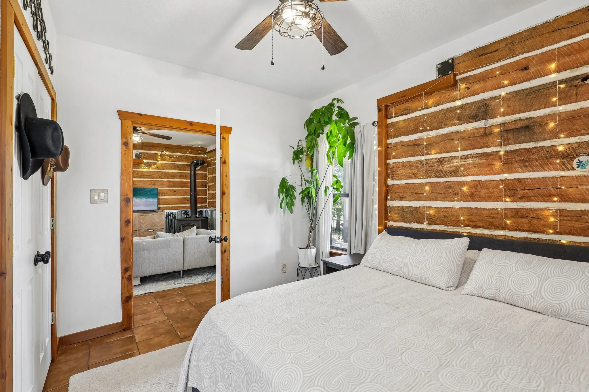 Bedroom featuring a prominent log wall accent, white walls, and a ceiling fan