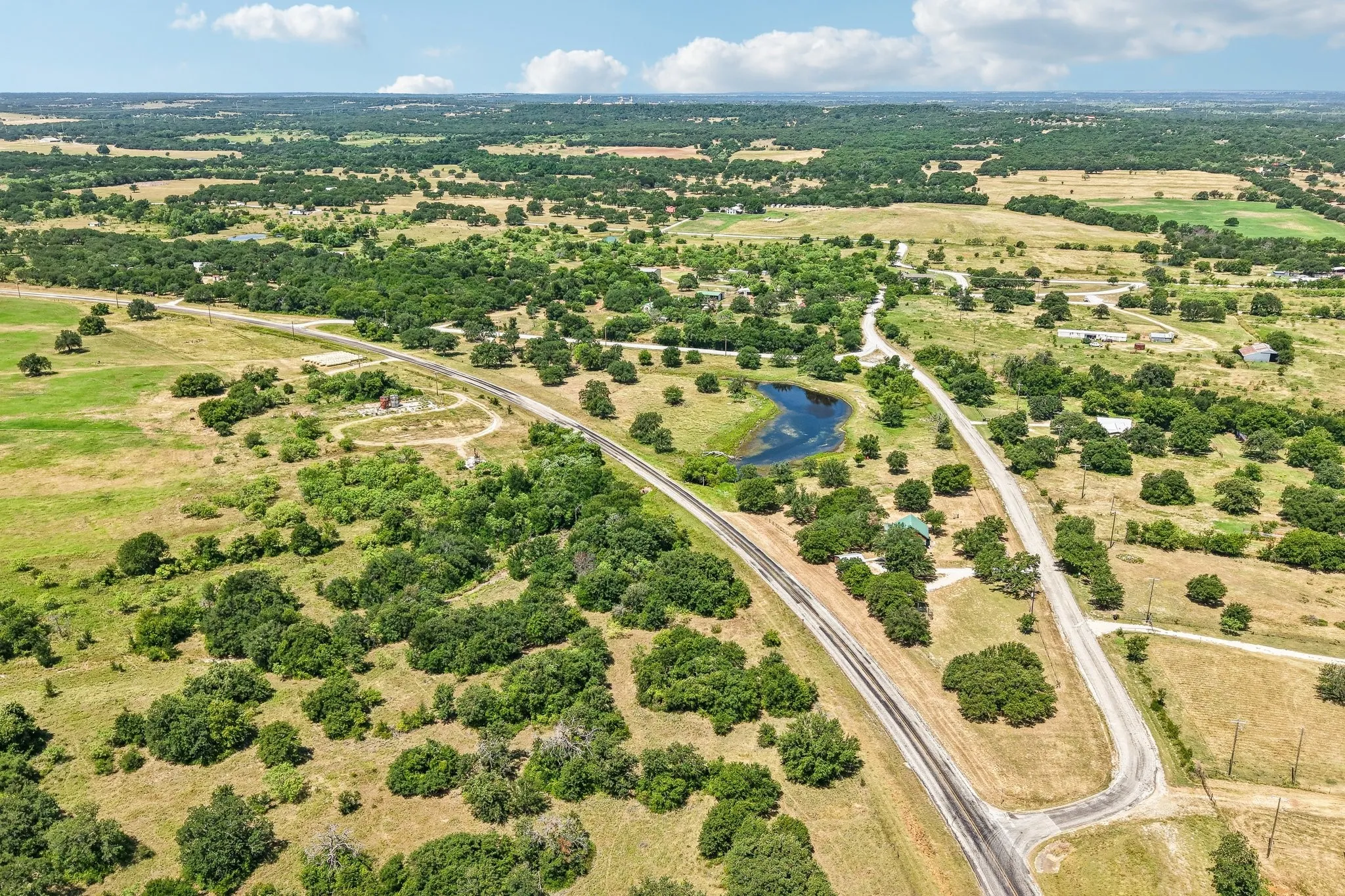 Expansive rural landscape featuring a private pond, mature trees, and a winding paved road