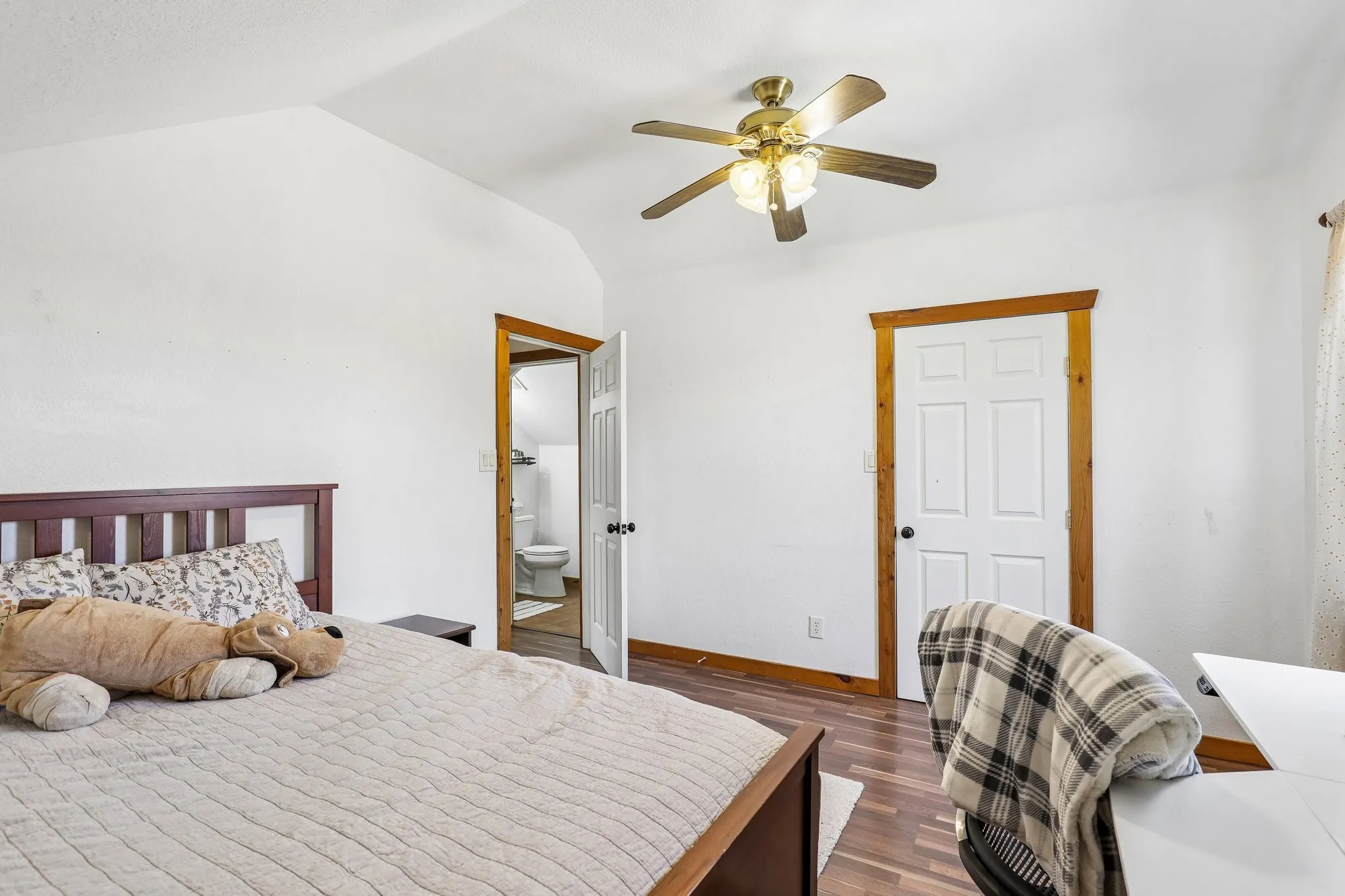 Vaulted ceiling bedroom with wood-finish flooring, a ceiling fan with integrated lighting, and a solid-core interior door with natural wood trim
