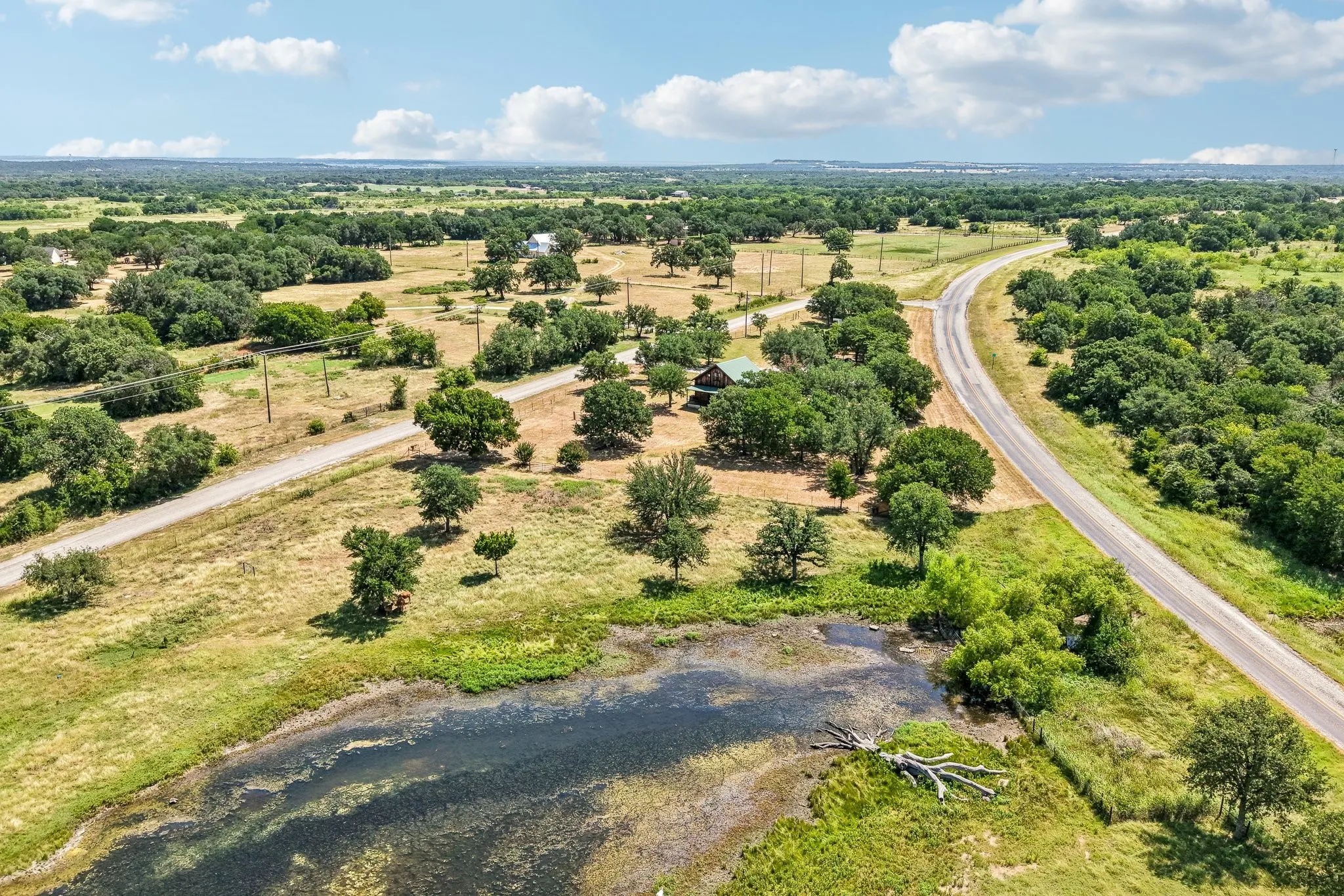 Expansive aerial property featuring a winding road, diverse tree coverage, and a natural pond
