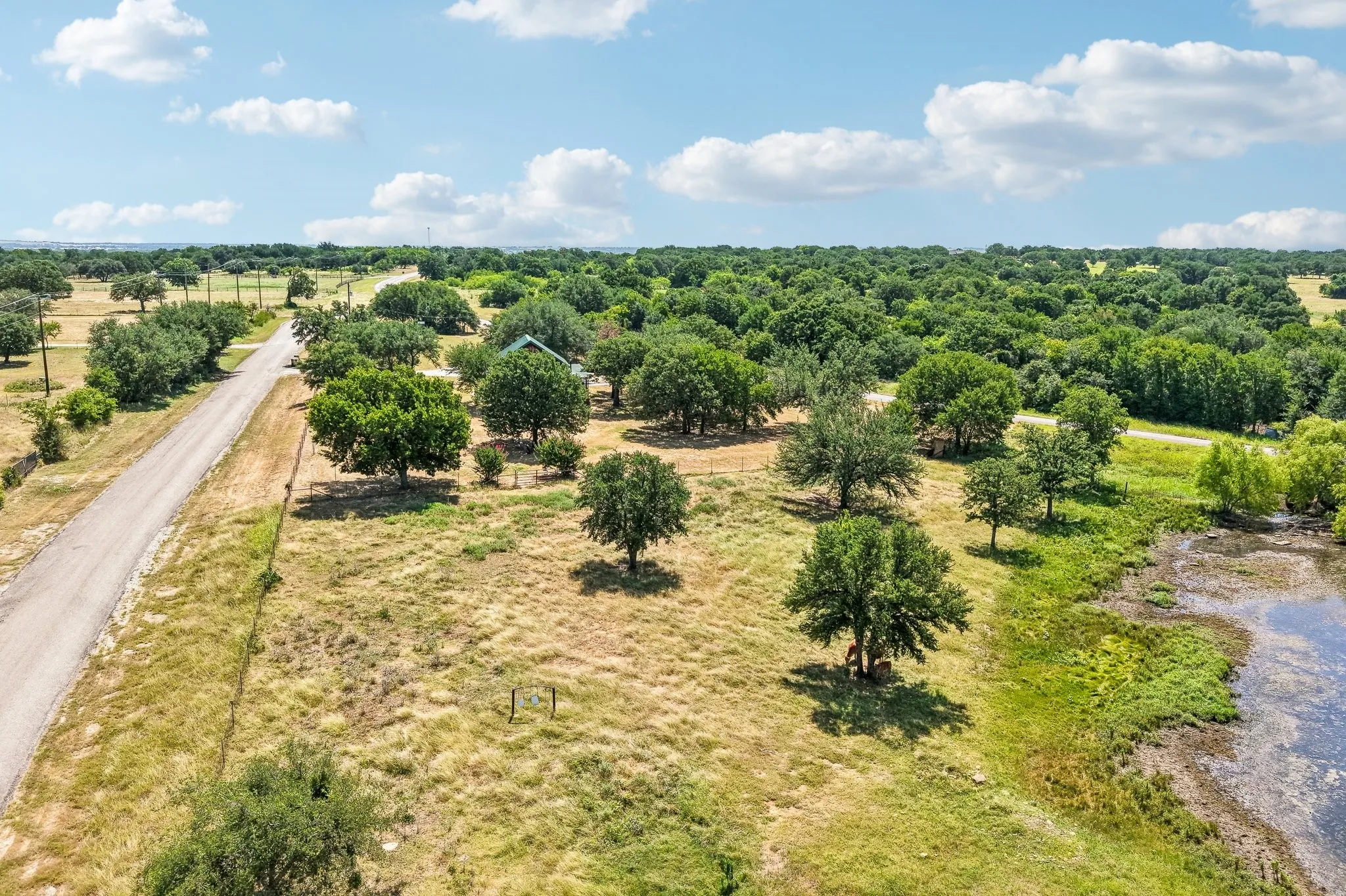 Expansive property featuring a private road, mature trees, a discernible structure, and a natural pond