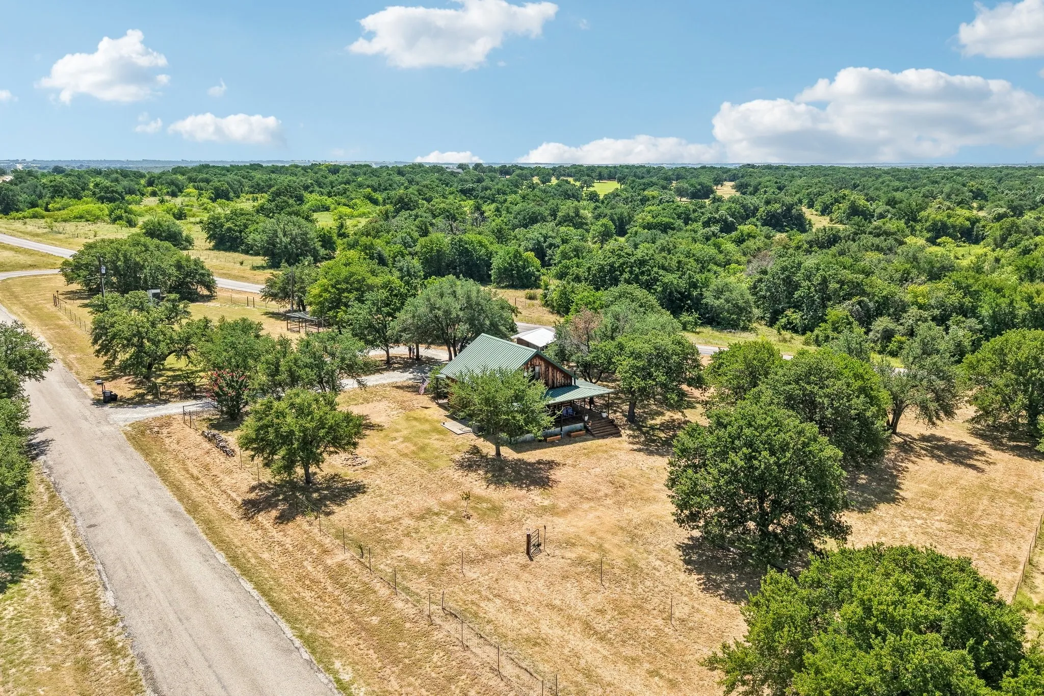 Wooded acreage featuring a single-story dwelling with a green roof, extensive tree canopy, and a visible road