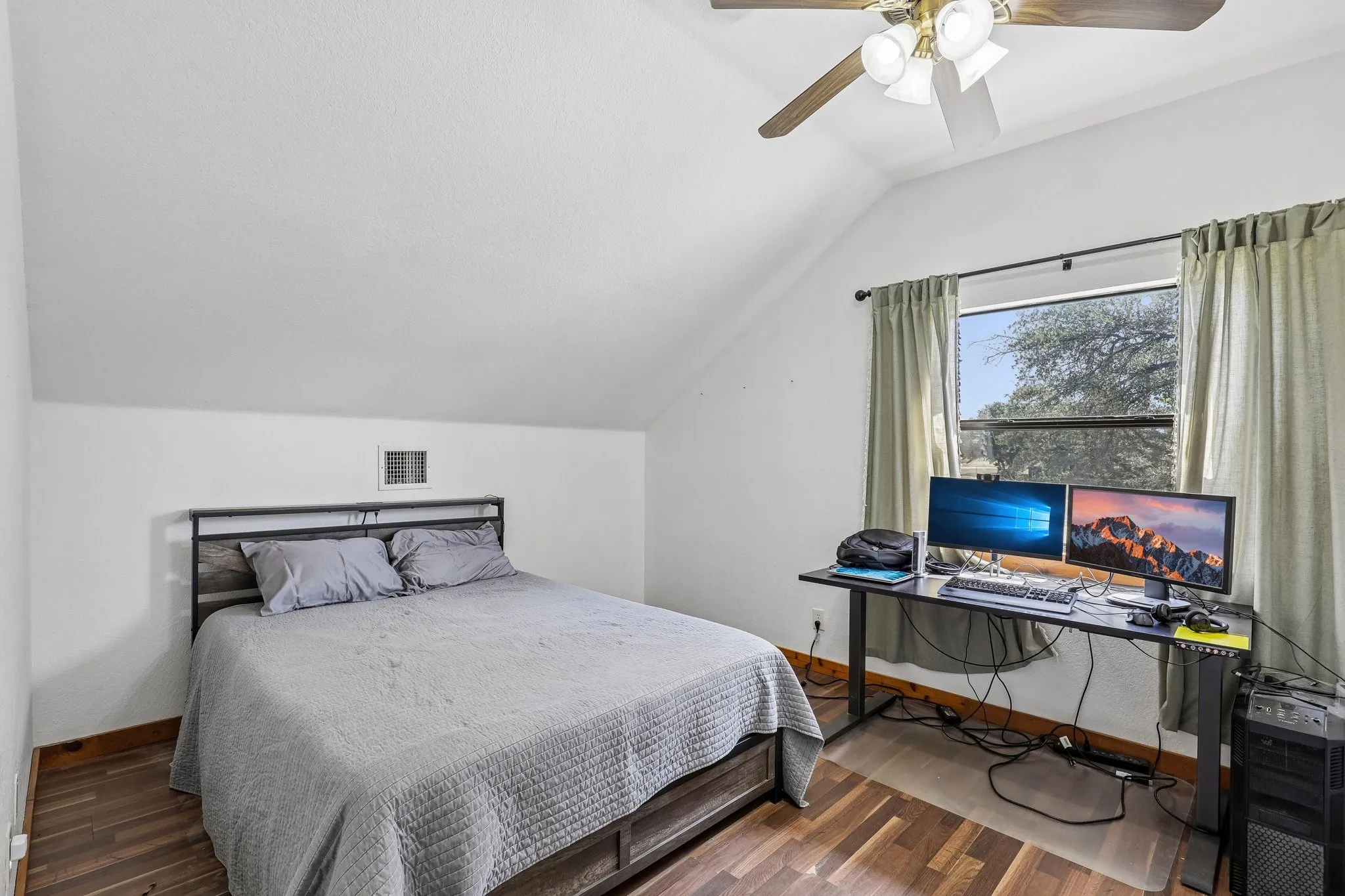 Vaulted ceiling bedroom featuring wood-finish flooring, a window with exterior views, and a ceiling fan with integrated lighting