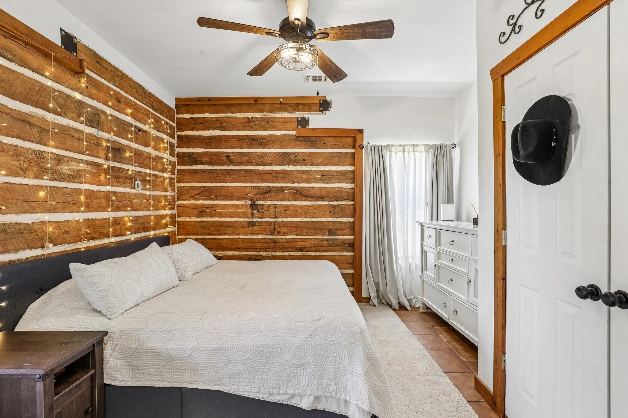 Interior room featuring wood-finish accent walls, a ceiling fan with integrated lighting, wood-finish flooring, a white interior door with dark hardware, and light-colored curtains