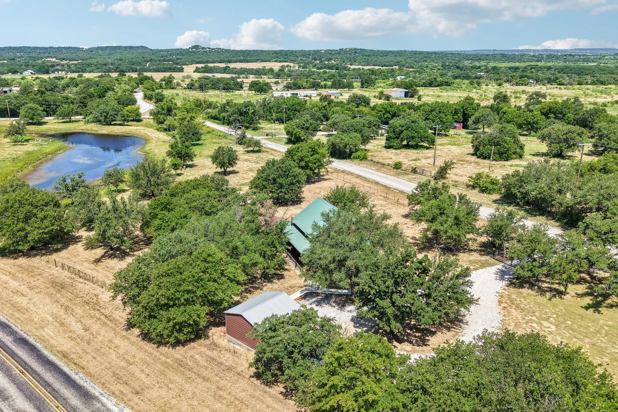 Expansive property featuring a private pond, mature trees, a main residence with a green roof, a separate red barn, and gravel driveways