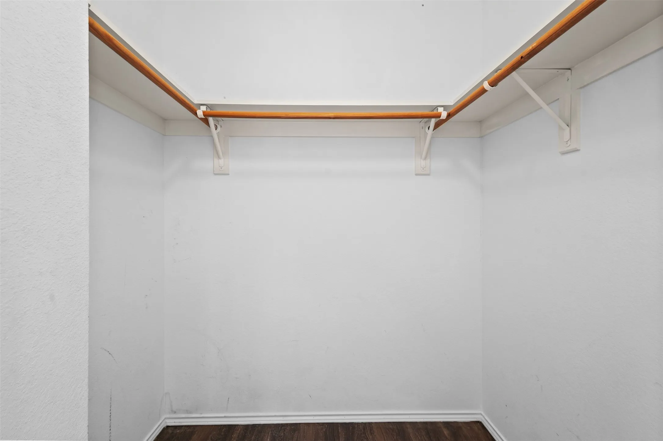 Reach-in closet featuring white walls, wood-finish flooring, and a corner shelving system with two wooden hanging rods