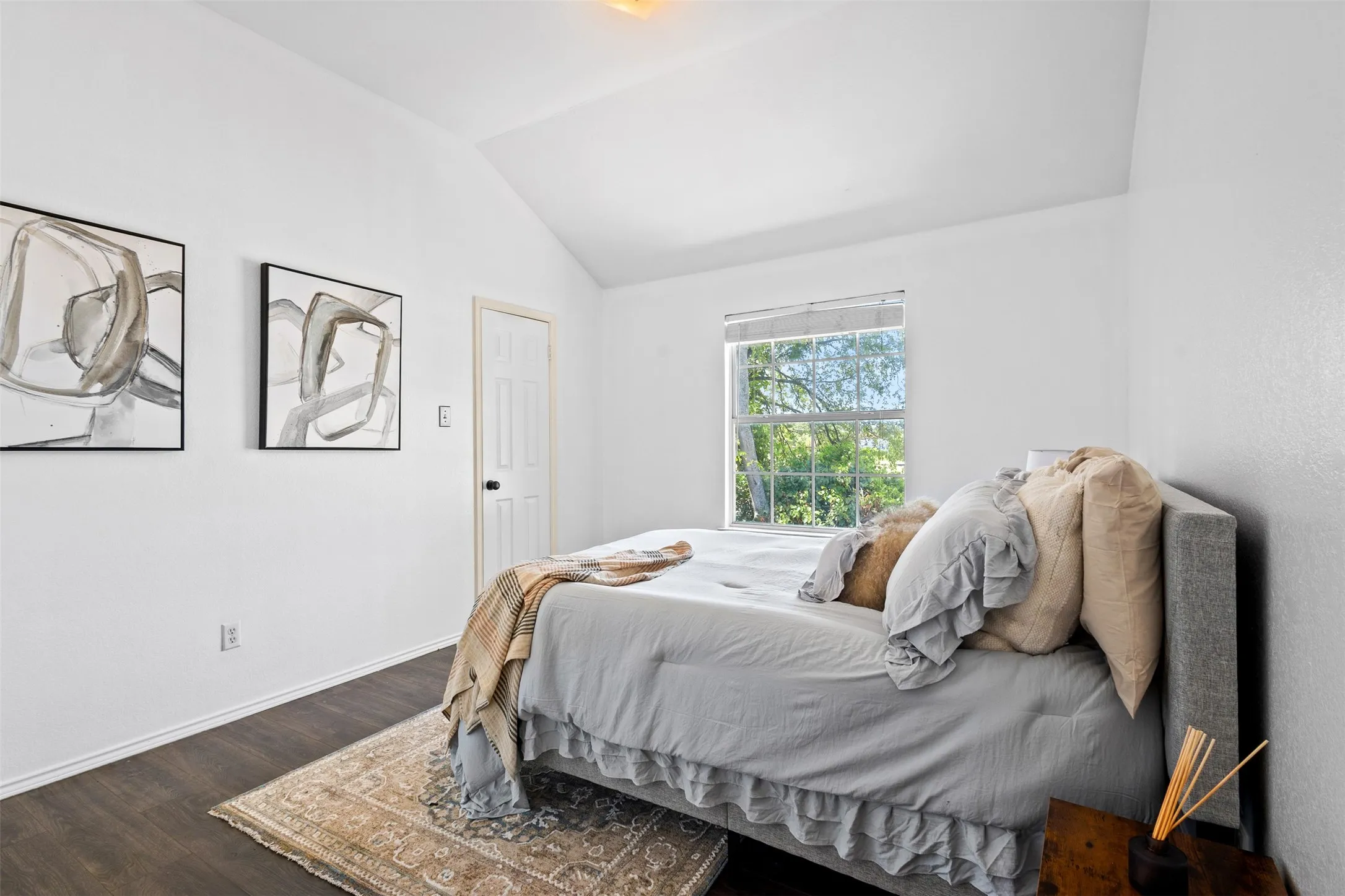 Vaulted ceiling bedroom featuring wood-finish flooring, a double window, and a paneled interior door
